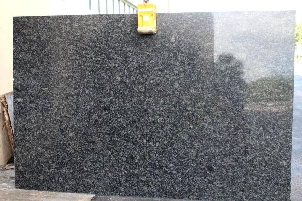 Large, polished dark gray granite slab with light flecks, suspended by a yellow clamp.