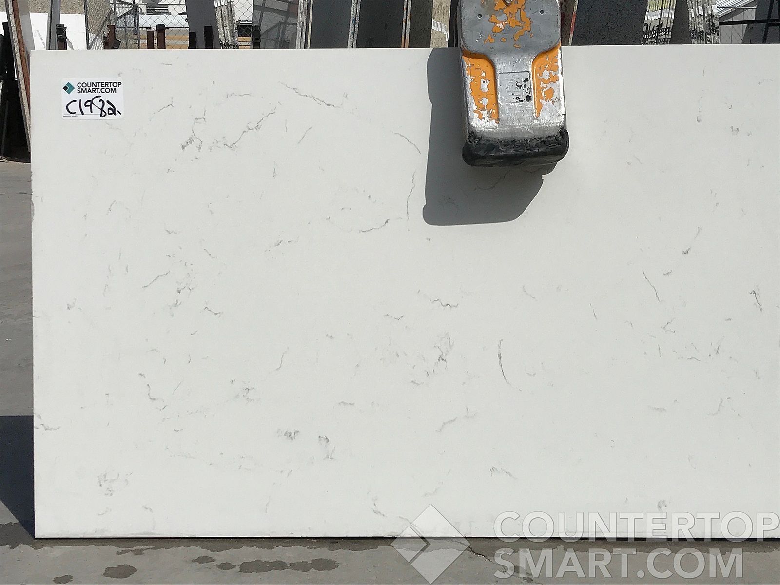 White countertop slab with subtle gray veining, held by machinery.