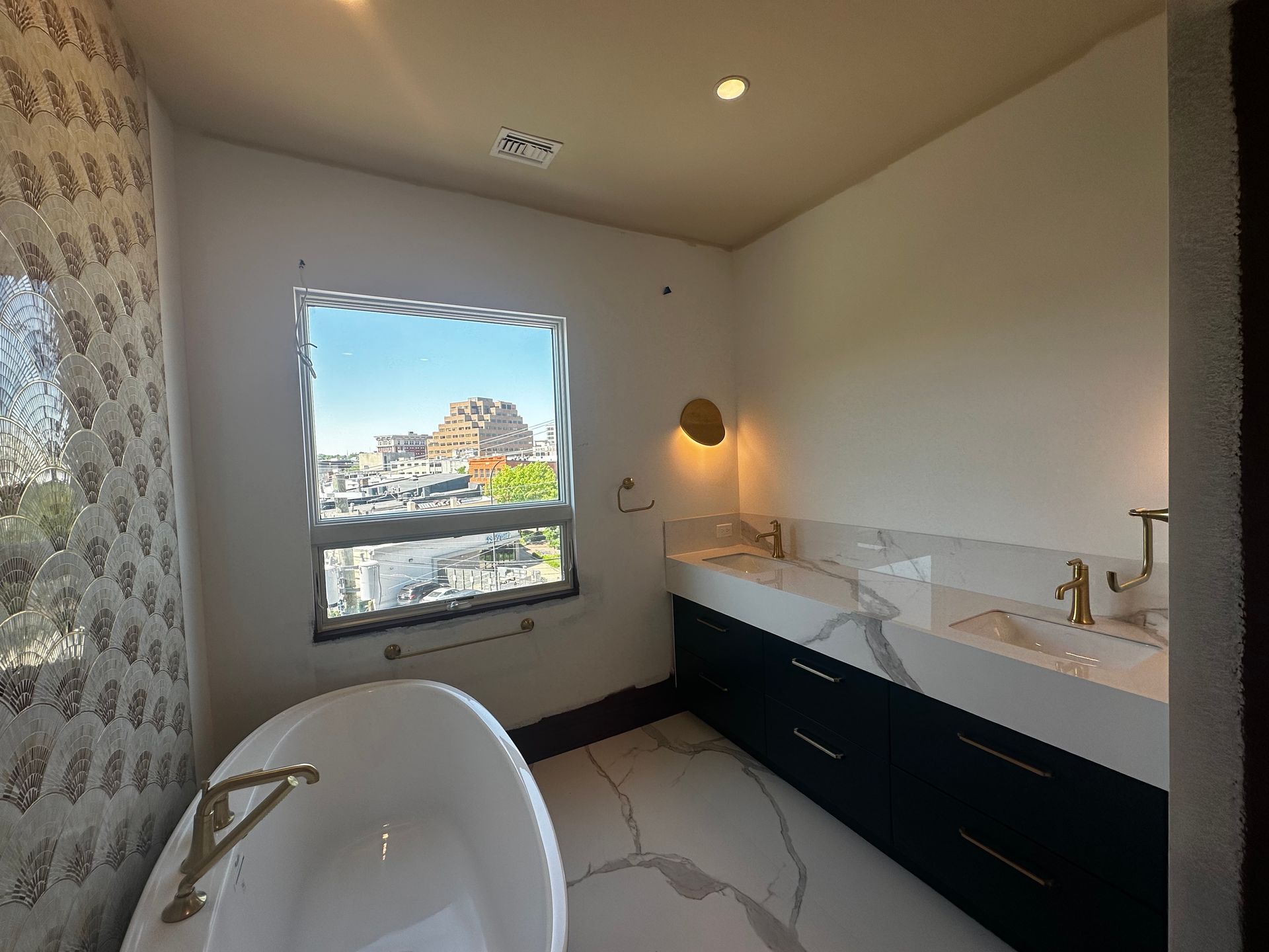Modern bathroom with bathtub, double vanity, and window view of rooftops