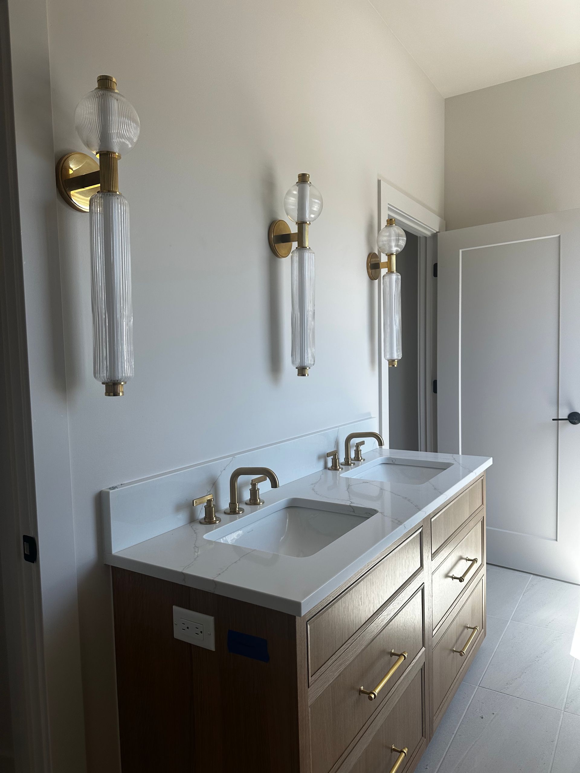 Bathroom vanity with double sinks, white countertop, wood cabinets, and wall sconces in a bright room