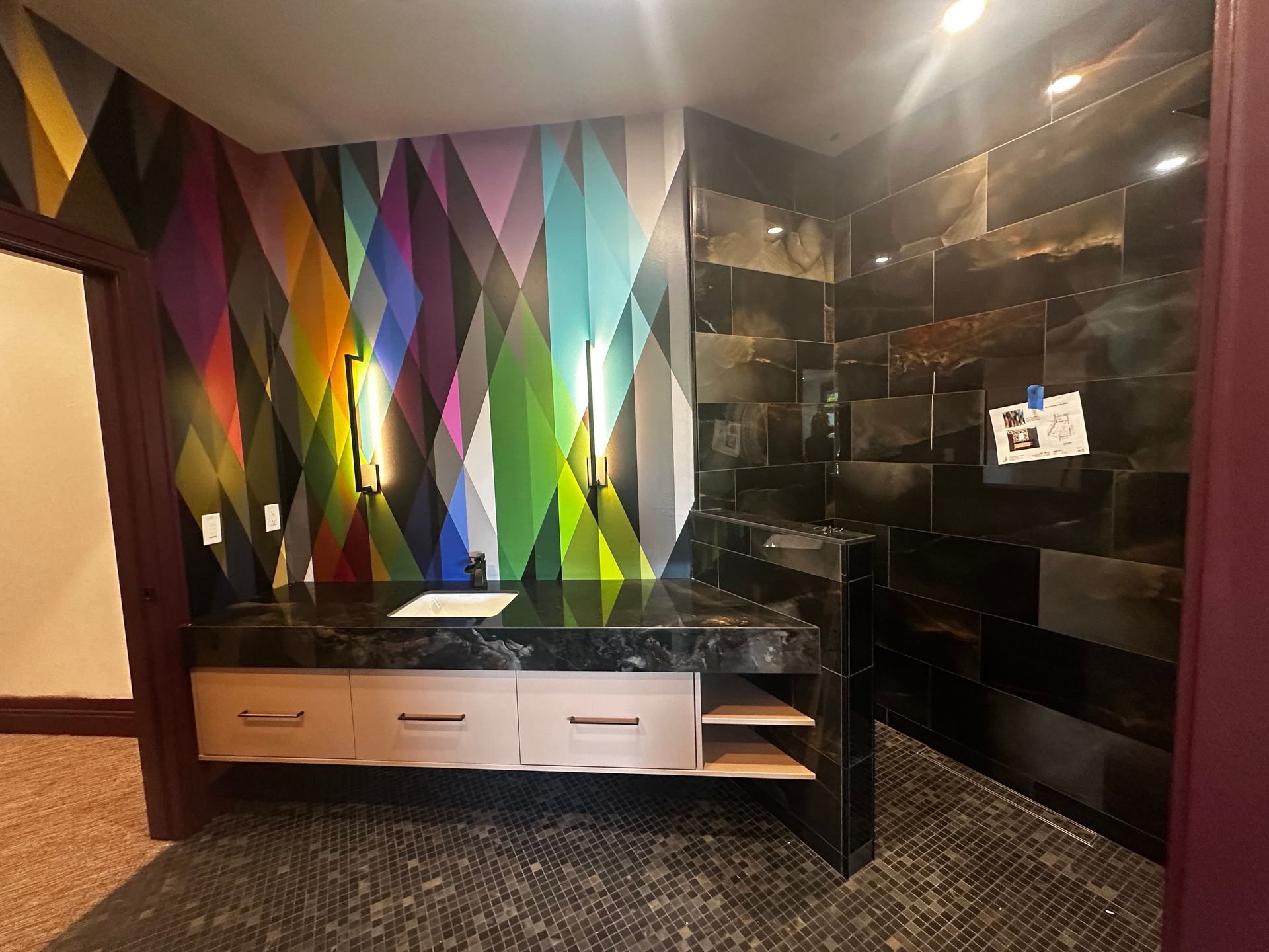 Modern room interior with colorful geometric wall panel, black cabinets, and mirrored wall lighting