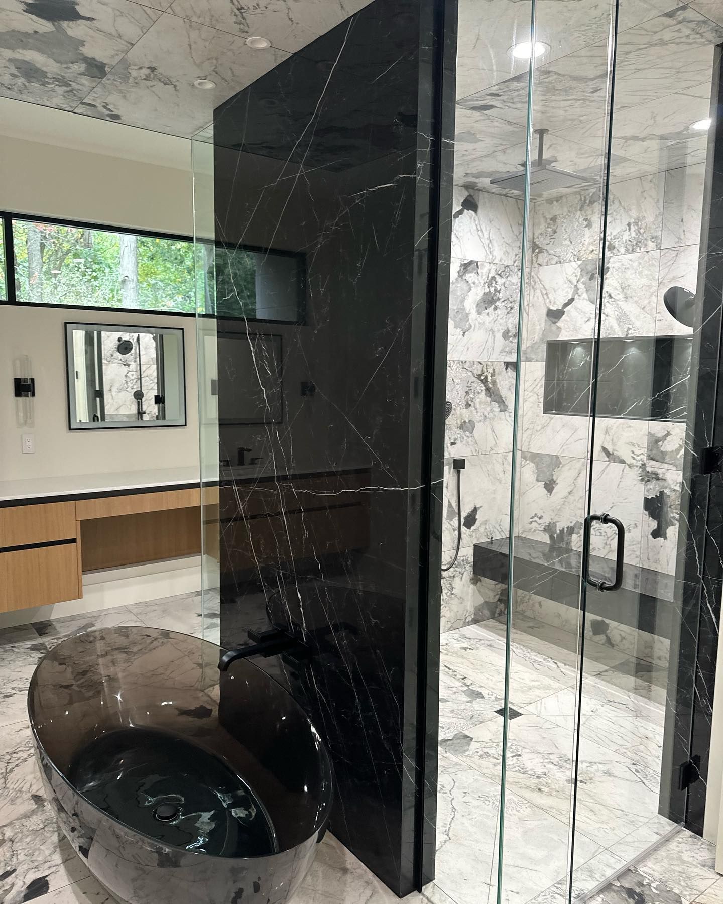 Modern bathroom with a black shower enclosure, glass doors, and marble walls beside a vanity area