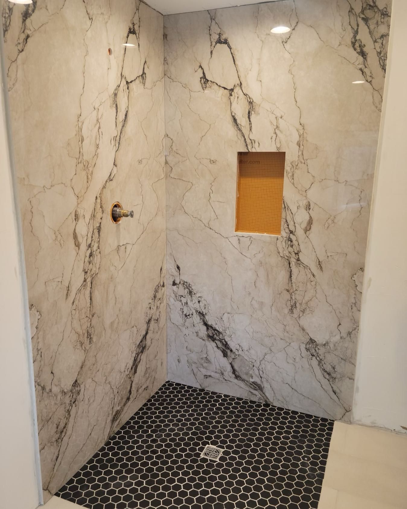 Marble-tiled shower stall with black mosaic floor and small recessed window
