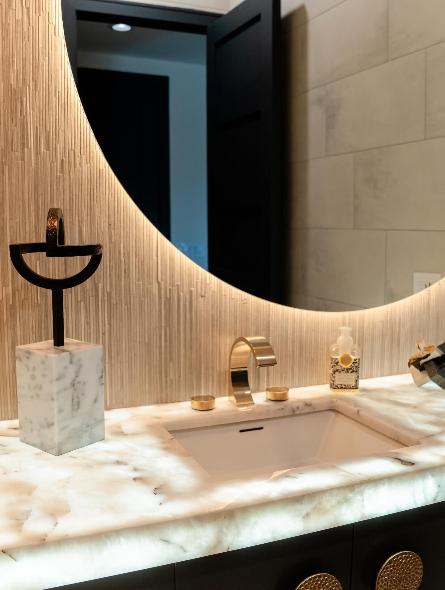 Marble bathroom vanity with gold faucet, circular mirror, and textured wood wall paneling