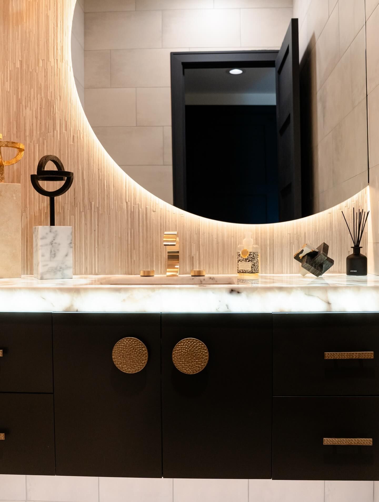 Elegant modern bathroom vanity with black cabinets, marble countertop, round mirror, and gold accents