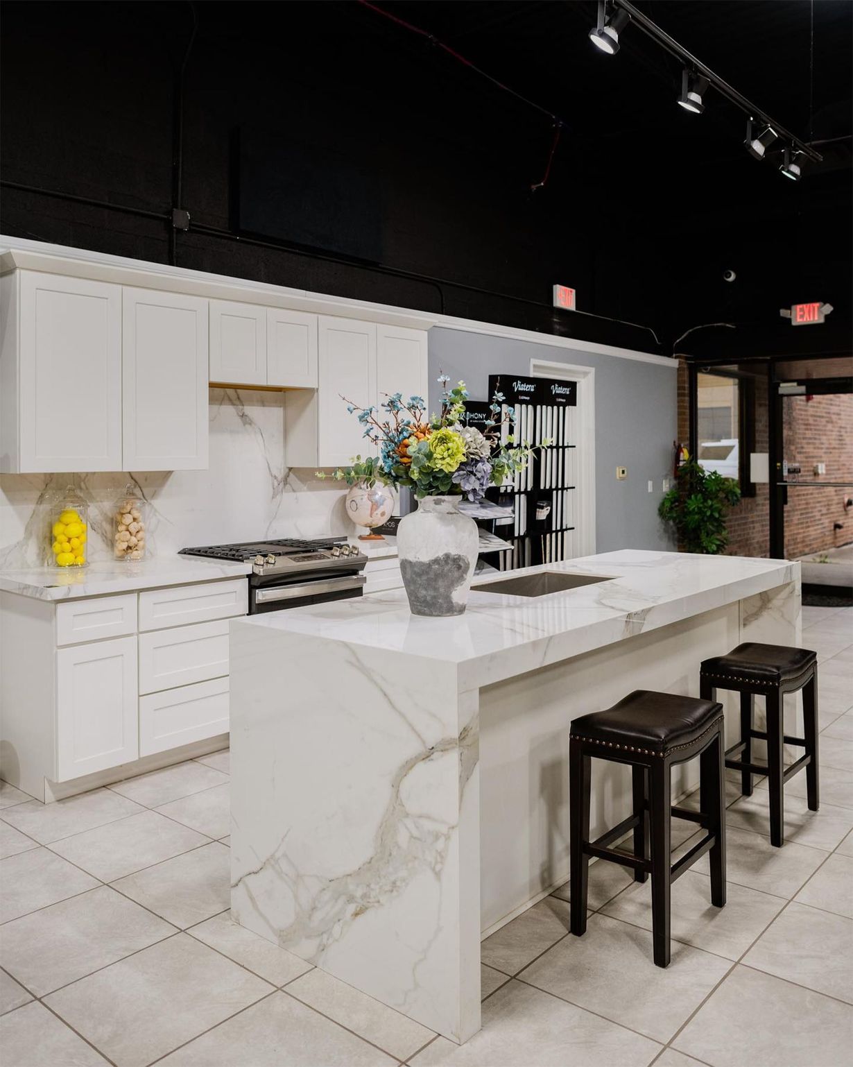 Modern white kitchen island with marble counters, bar stools, and floral centerpiece in a showroom