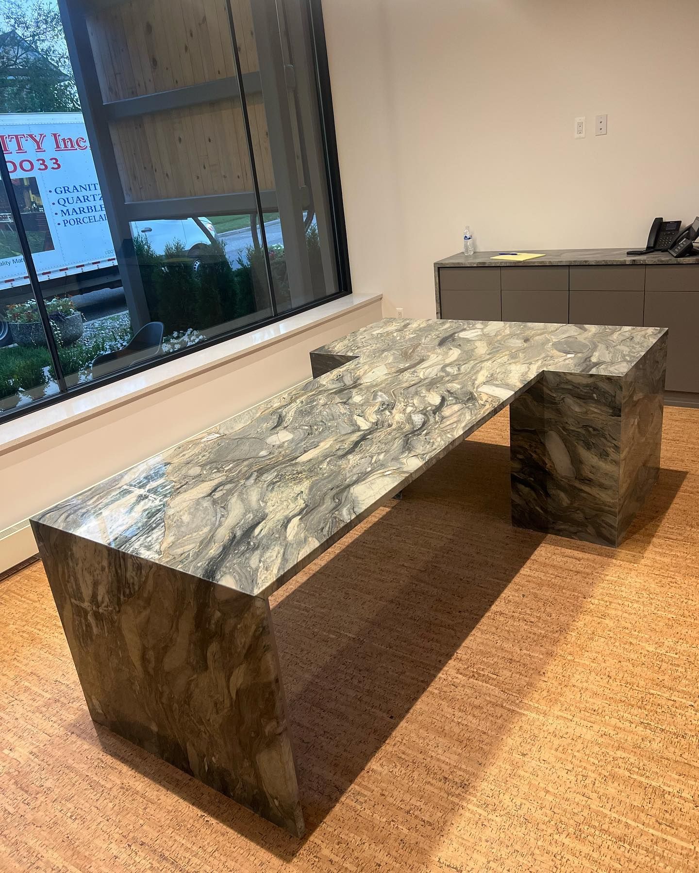 Marble bench in a modern office near a large window, with a small cabinet in the background.