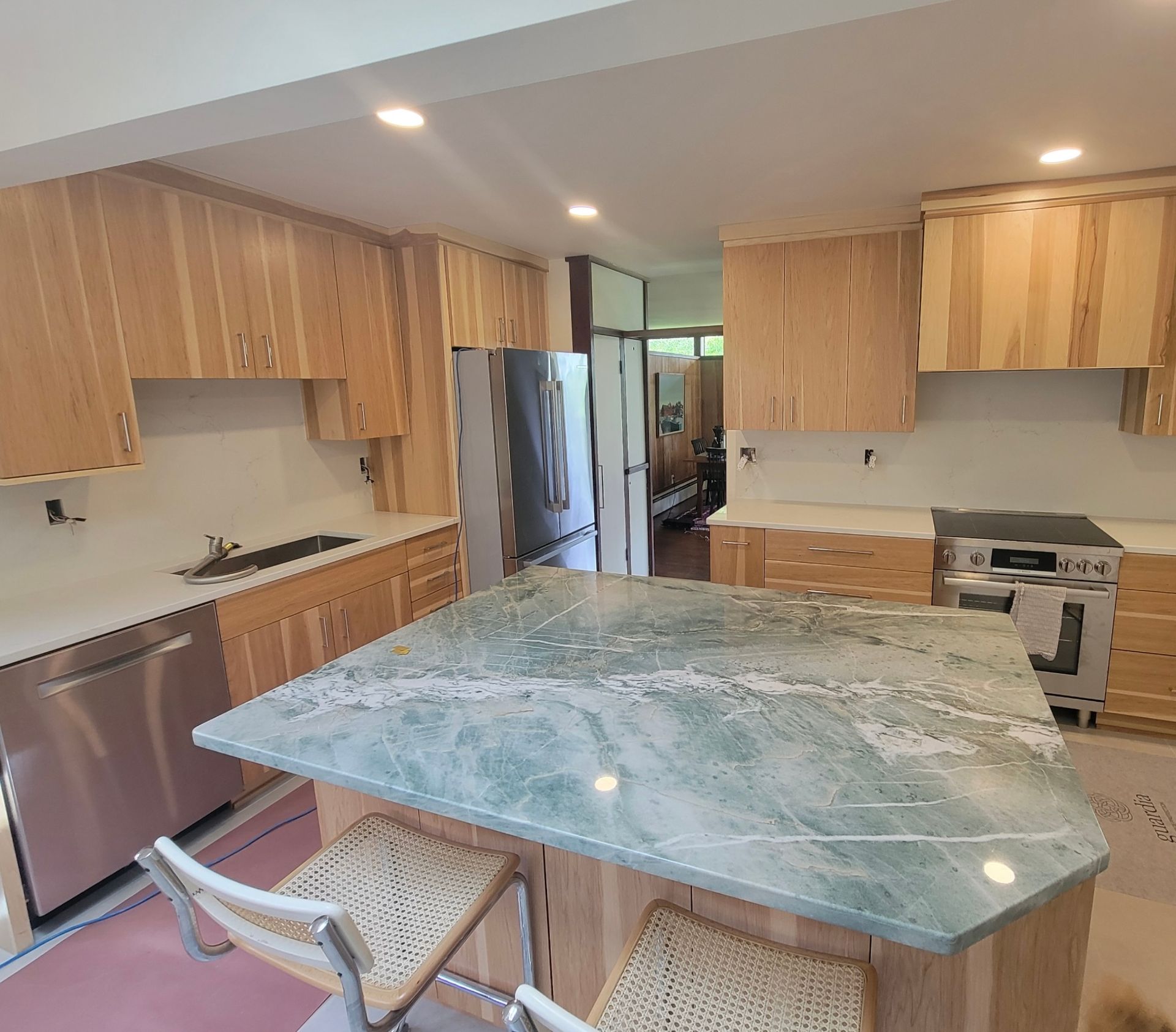 Modern kitchen with wood cabinets, stainless appliances, and a large green marble island with a stool.