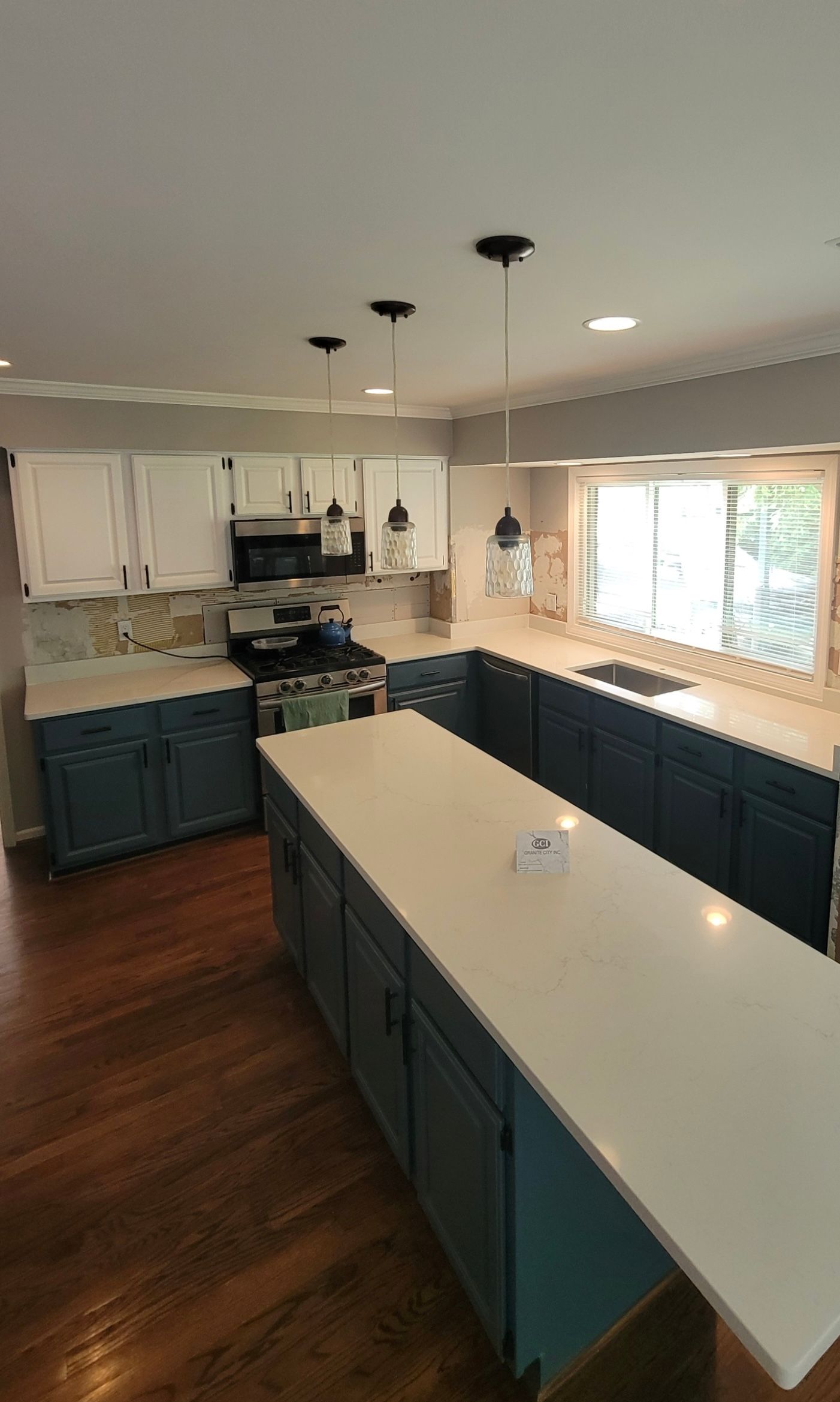 Bright kitchen with dark blue cabinets, white island, and large window over hardwood floors.