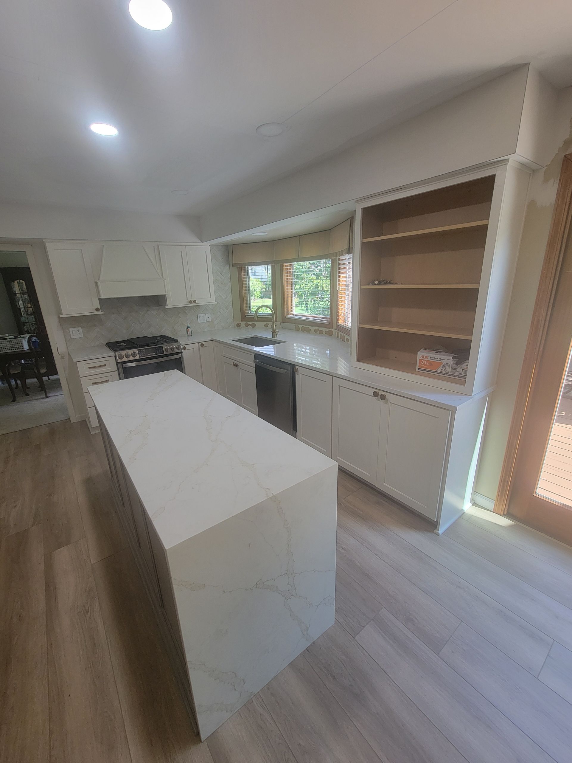 Modern kitchen with white island, built-in cabinets, wood flooring, and large windows