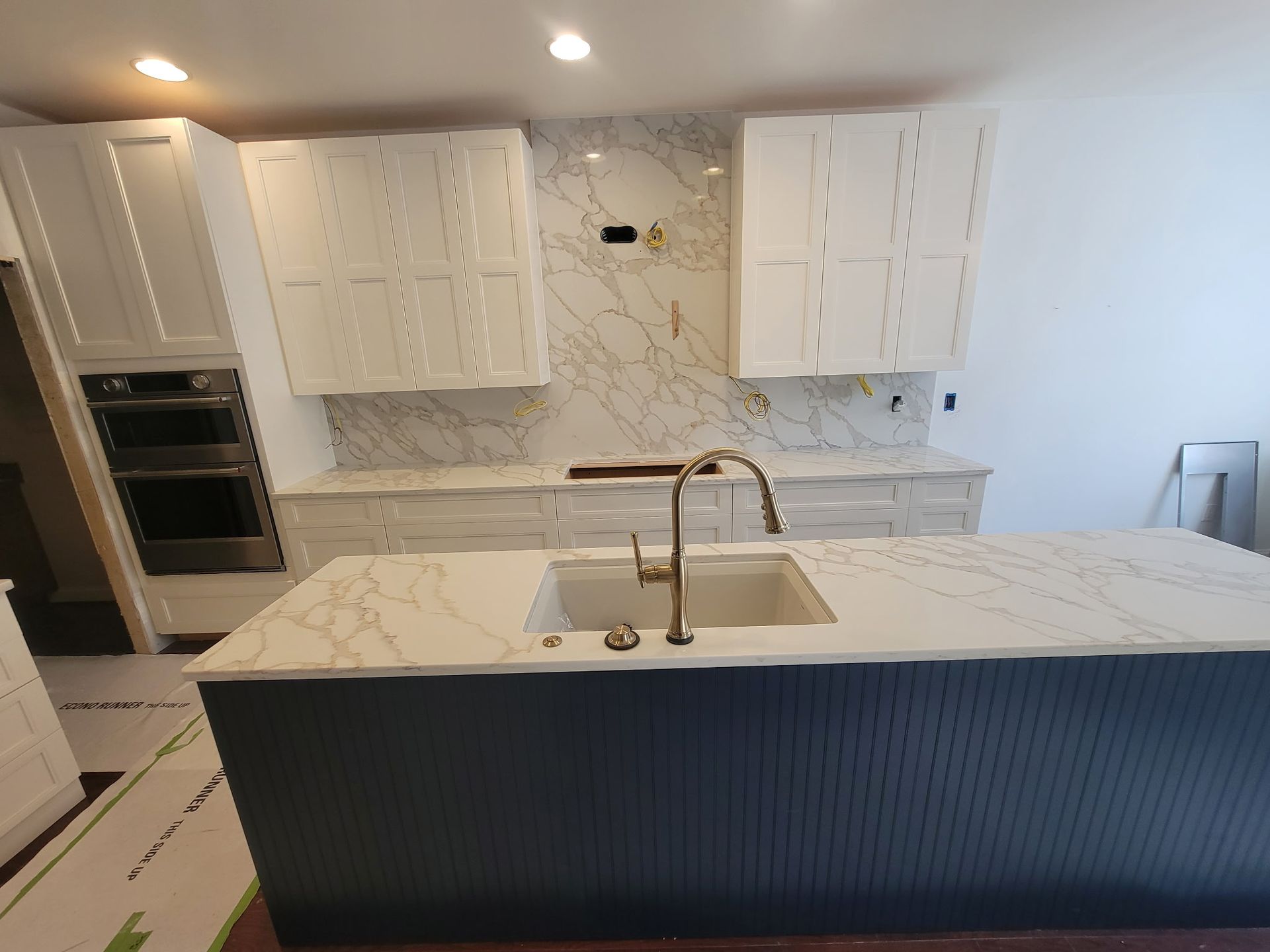 Modern white kitchen with marble island, dark blue island panel, and stainless steel sink and faucet