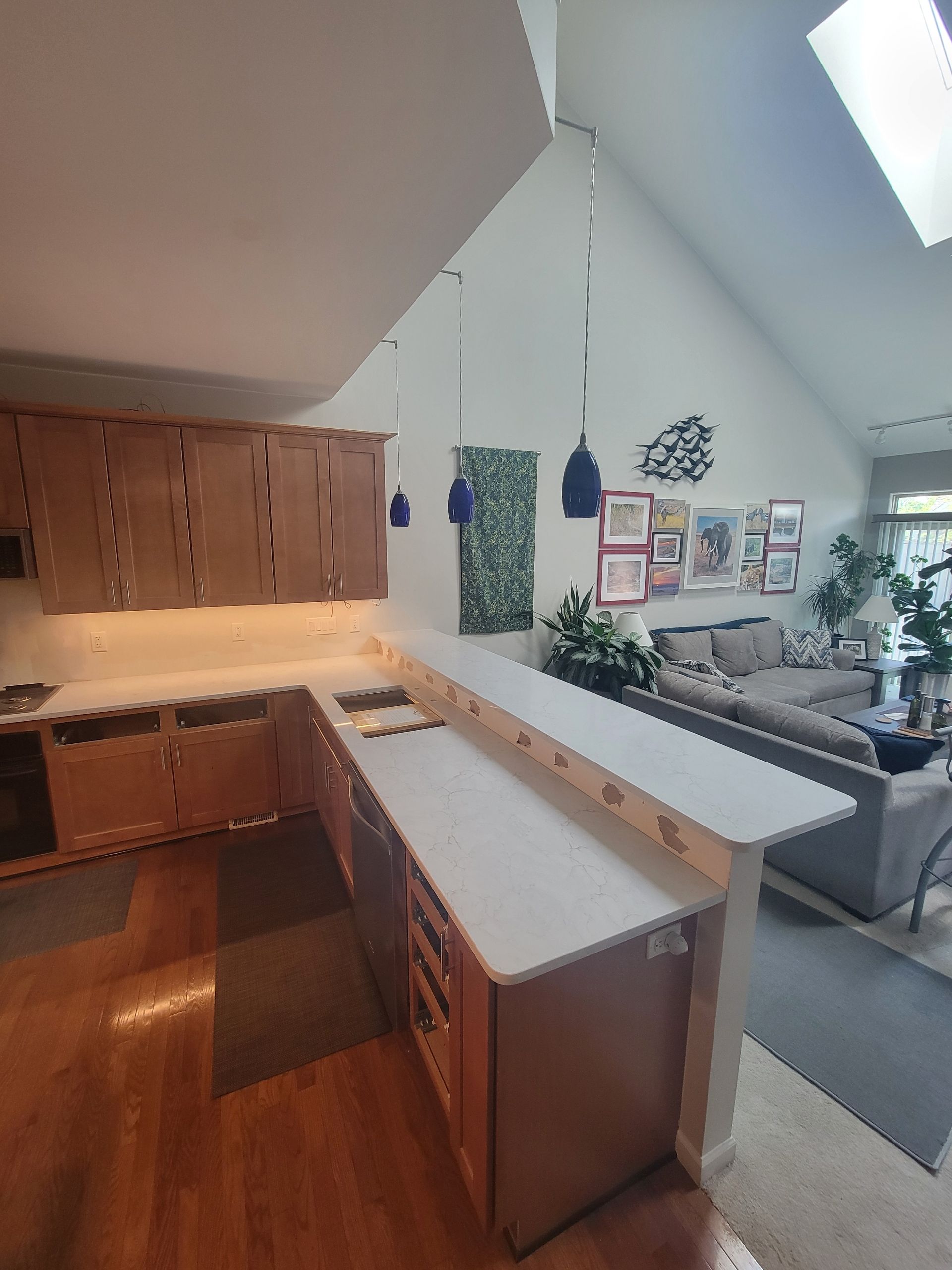 Kitchen interior with wood cabinets, white island, hardwood floors, skylight, and stair railing to living area