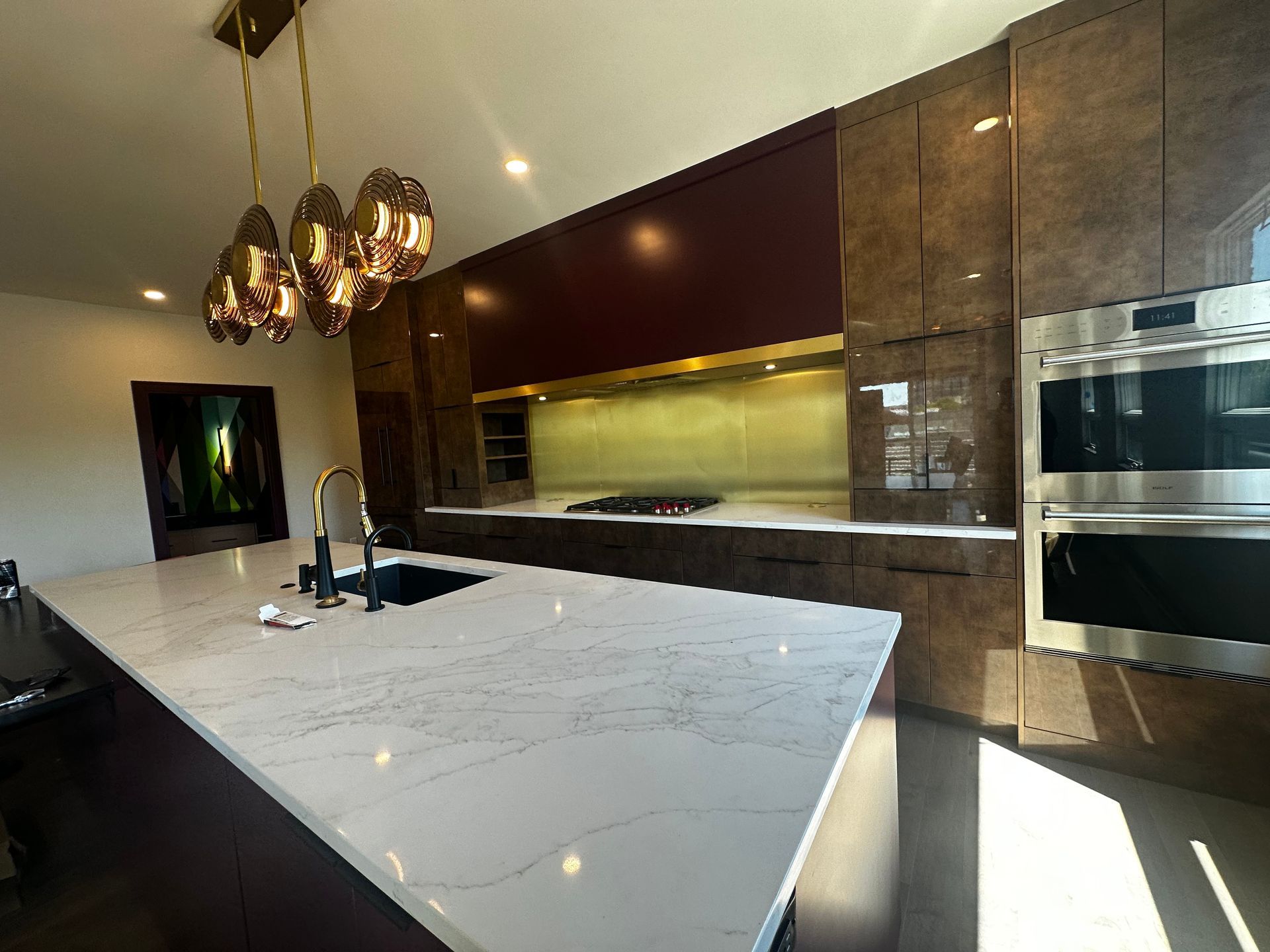 Modern kitchen with white marble island, brass pendant lights, wood cabinets, and built-in appliances