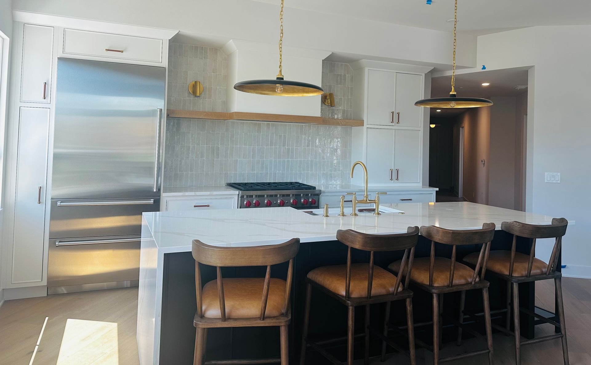 Bright modern kitchen with white cabinets, stainless fridge, island, and wooden stools
