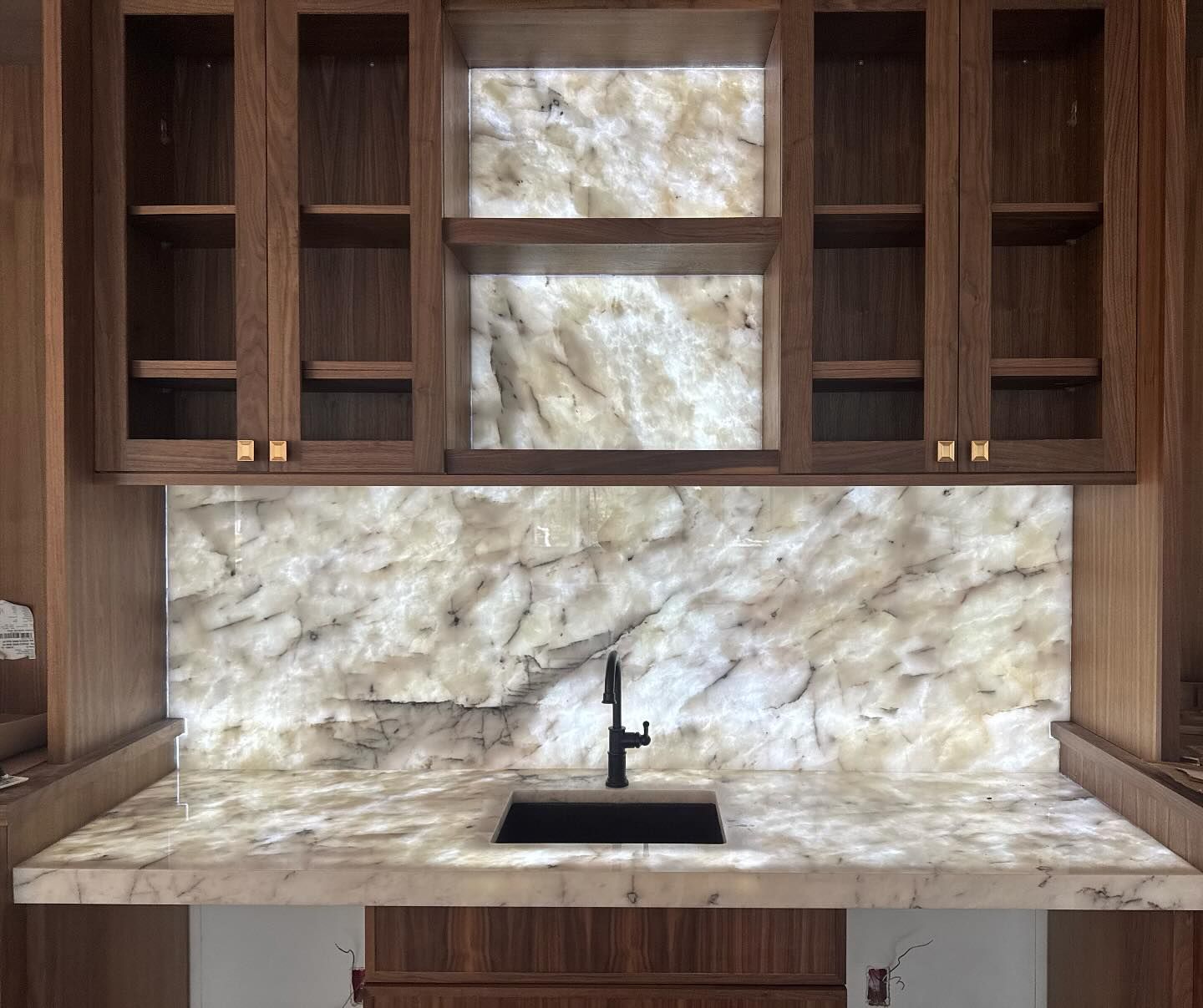 Built-in wooden shelves and cabinets framing a marble vanity with a black faucet and sink niche.
