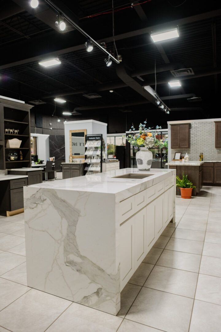 Modern kitchen showroom with a white island, tiled floor, and shelving under black ceiling lights