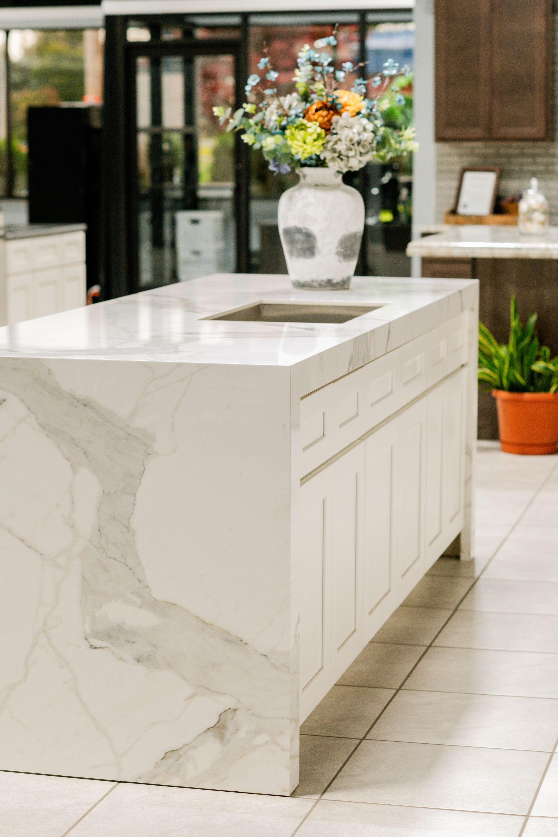 Modern kitchen island with white marble waterfall countertop and a vase of flowers
