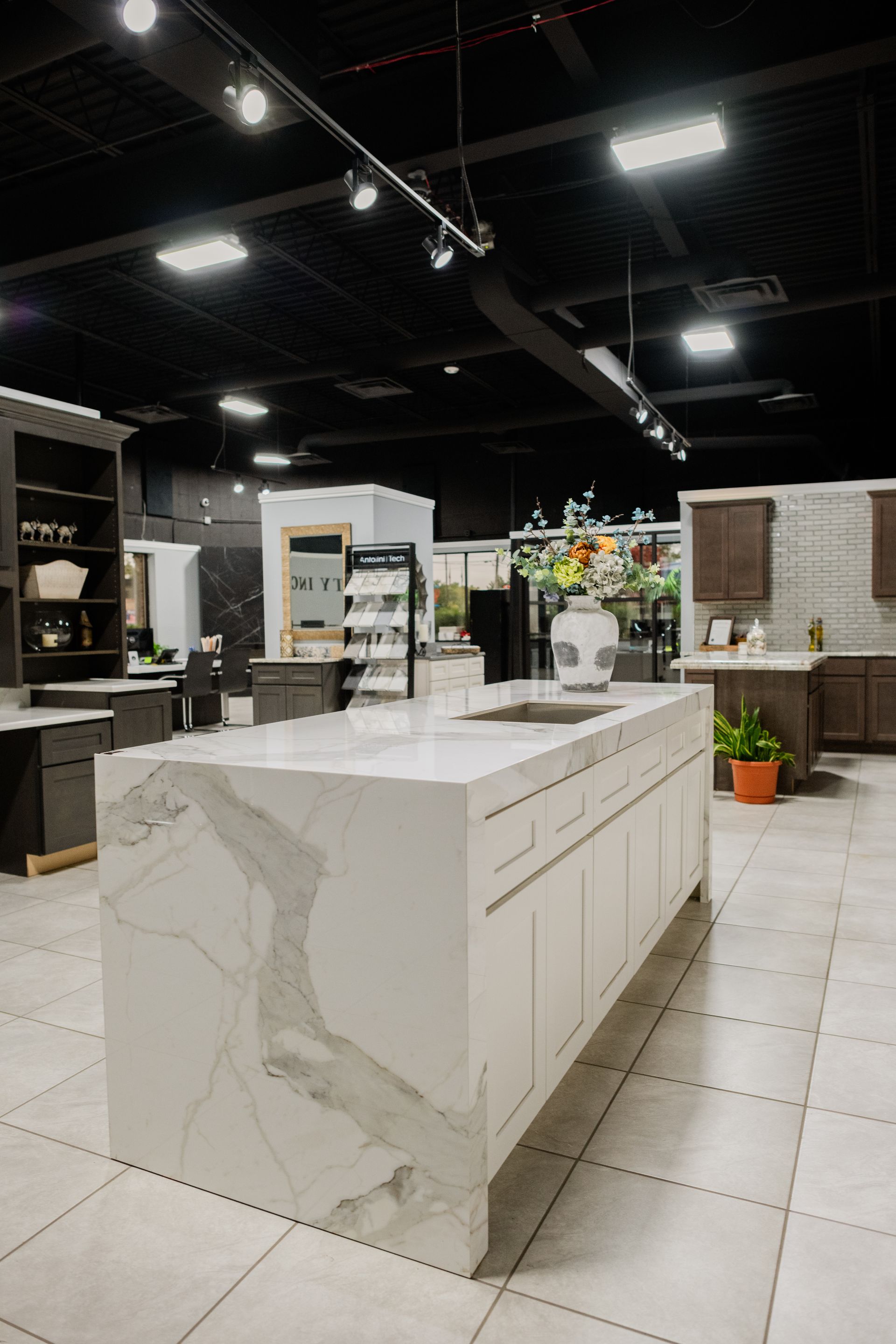 Modern showroom kitchen with a white marble island, tiled floor, and dark ceiling lighting
