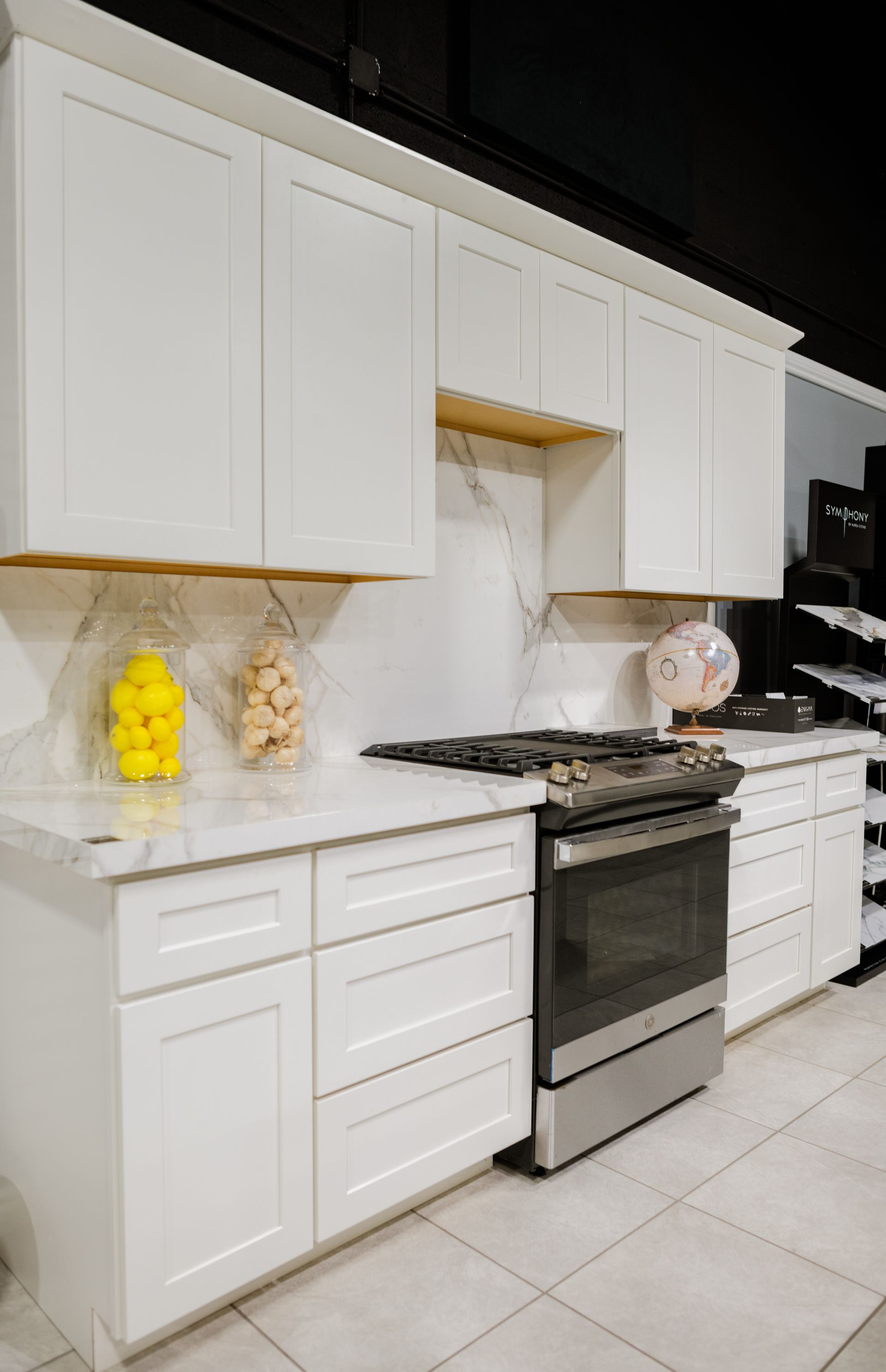 Modern white kitchen with cabinets, marble backsplash, gas stove, and tiled floor