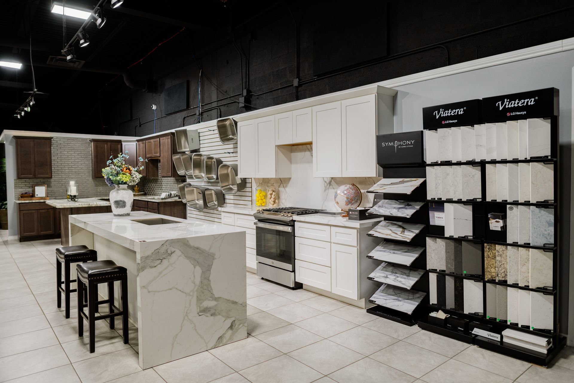 Modern kitchen showroom with white cabinets, marble island, bar stools, and display shelving
