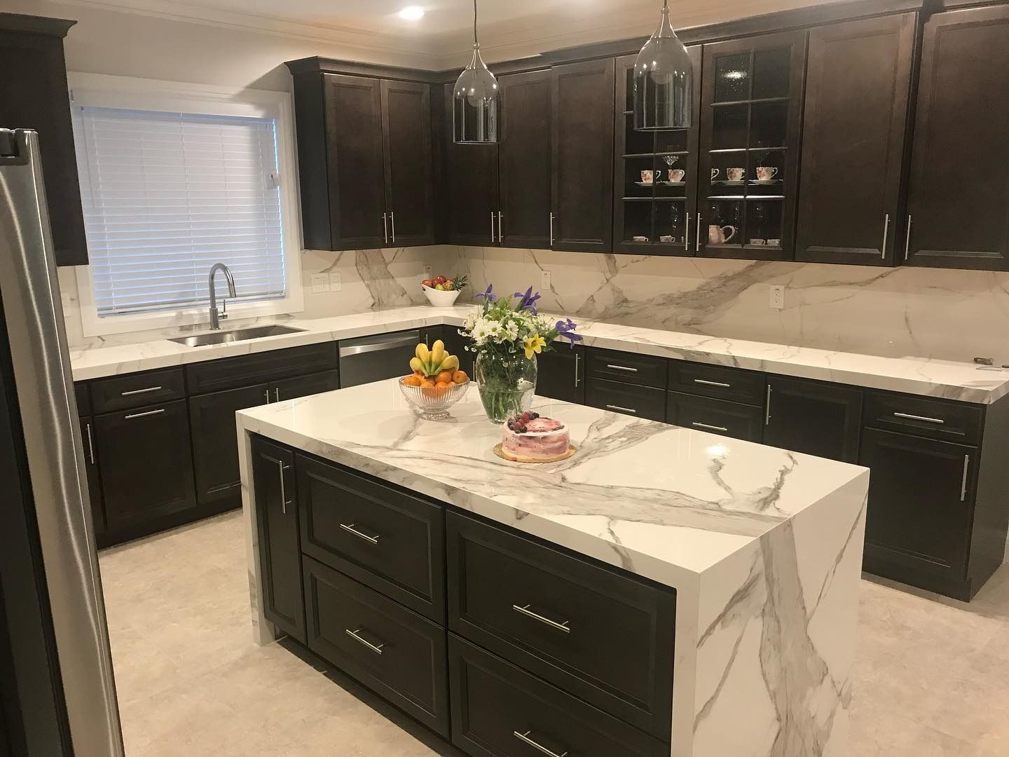 Modern kitchen with dark cabinets, white marble island, and flowers on the countertop.