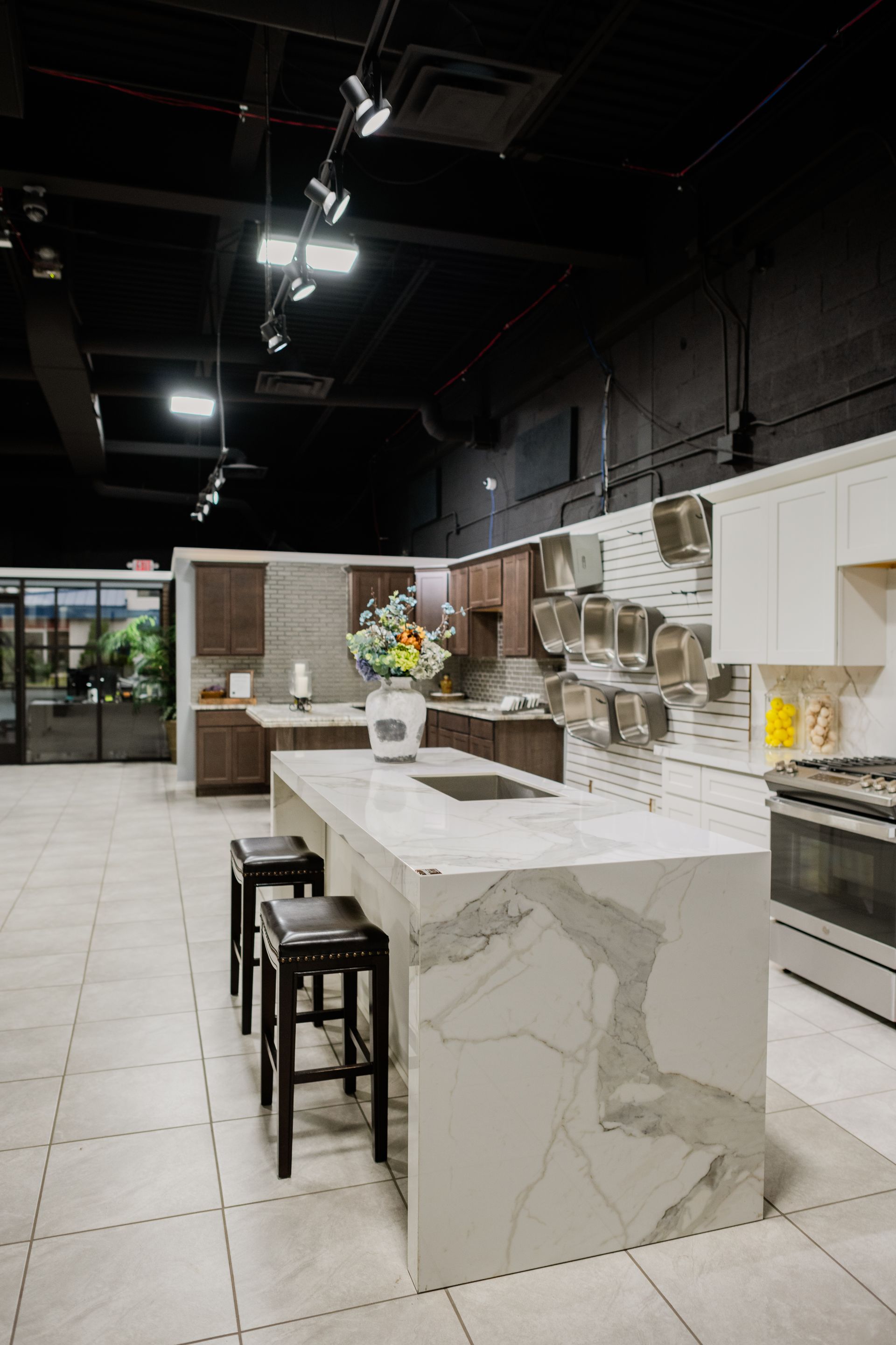 Modern kitchen showroom with marble island, stools, and appliances under bright ceiling lights