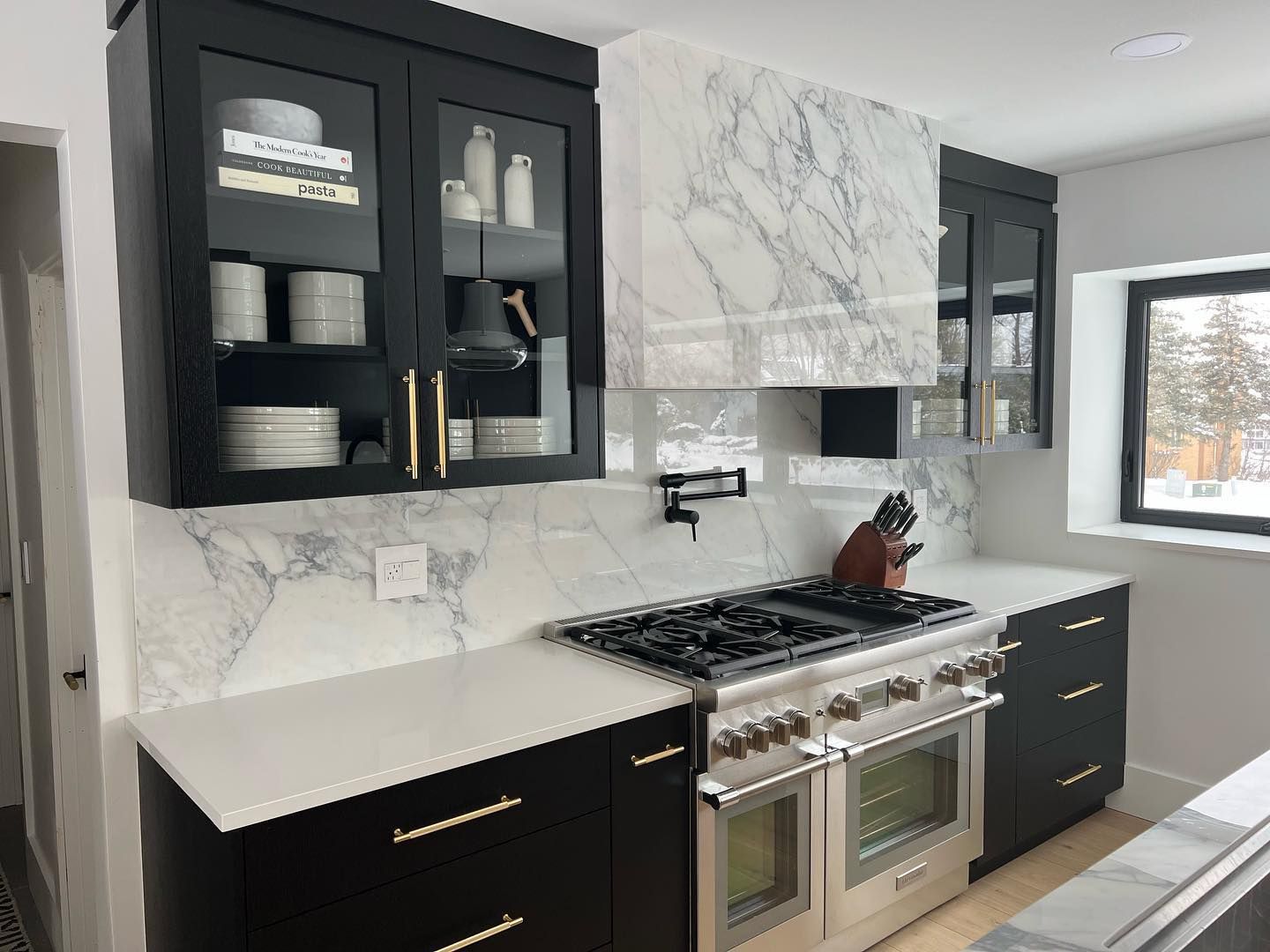 Modern kitchen with black cabinets, white marble backsplash, and stainless steel range under a marble hood