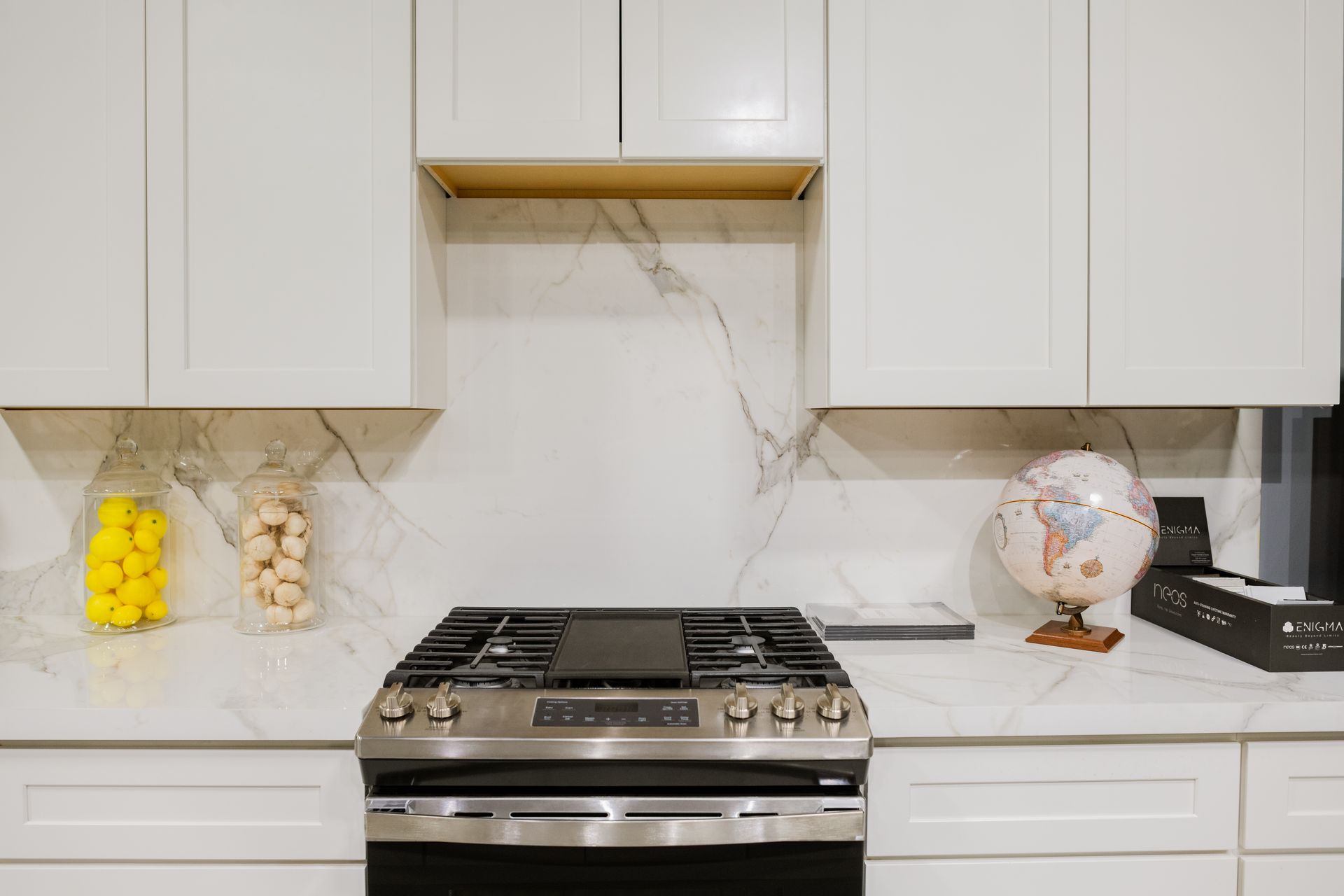 Modern kitchen with white cabinets, marble backsplash, gas range, and decorative jars and globe on the counter