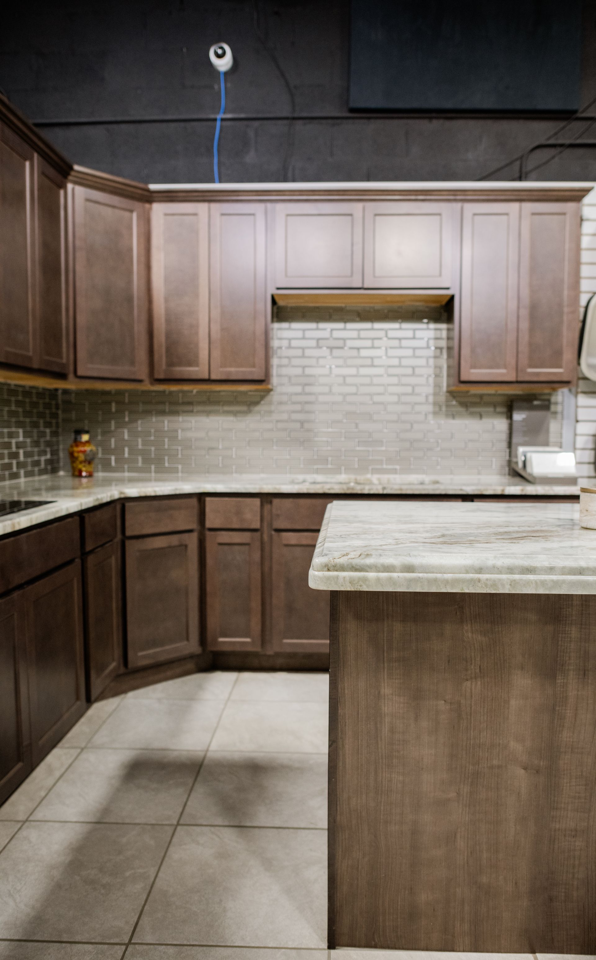 Modern kitchen with wood cabinets, beige tile floor, white backsplash, and a large island countertop.