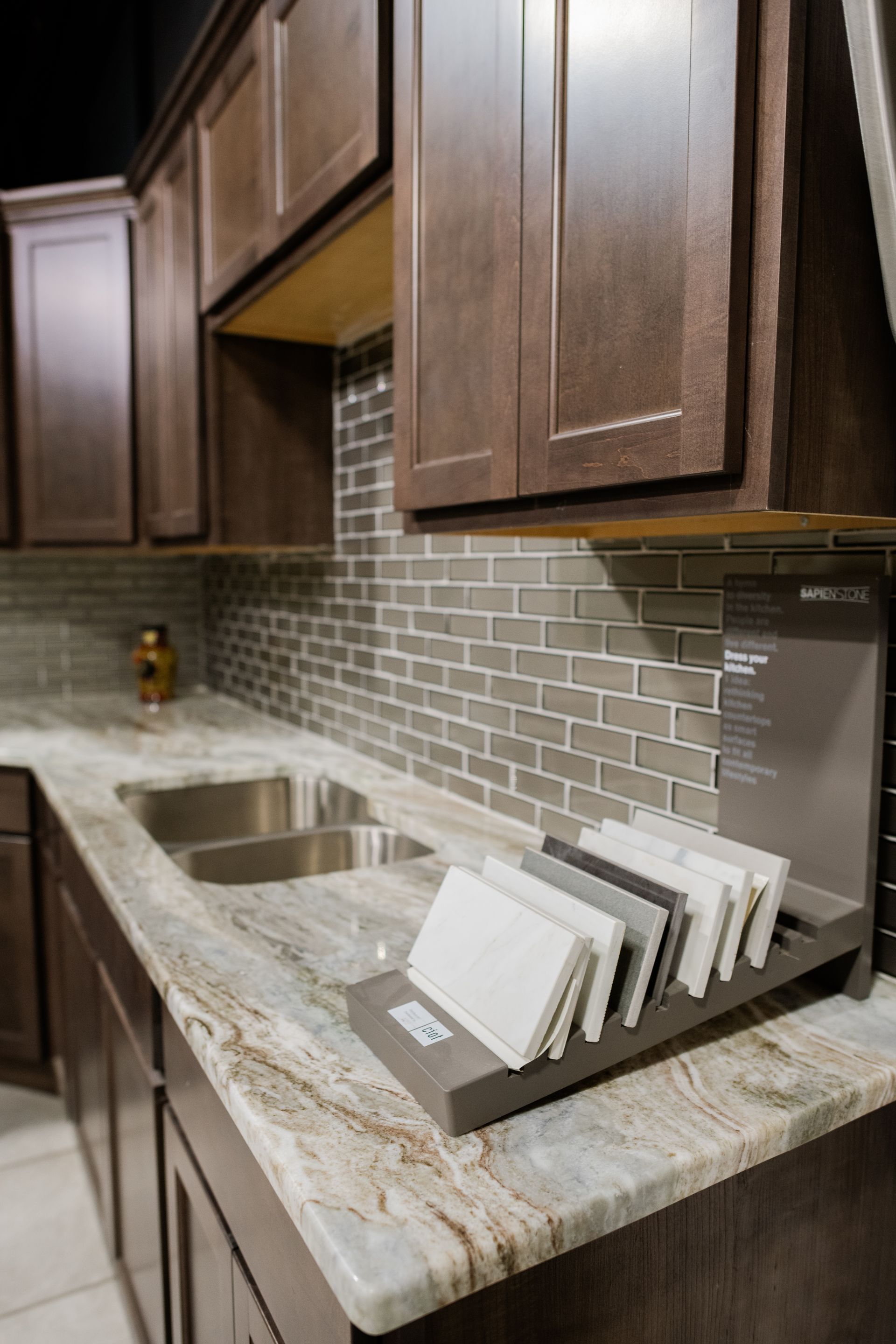 Modern kitchen countertop with sink, dark wood cabinets, gray tile backsplash, and a dish rack with plates