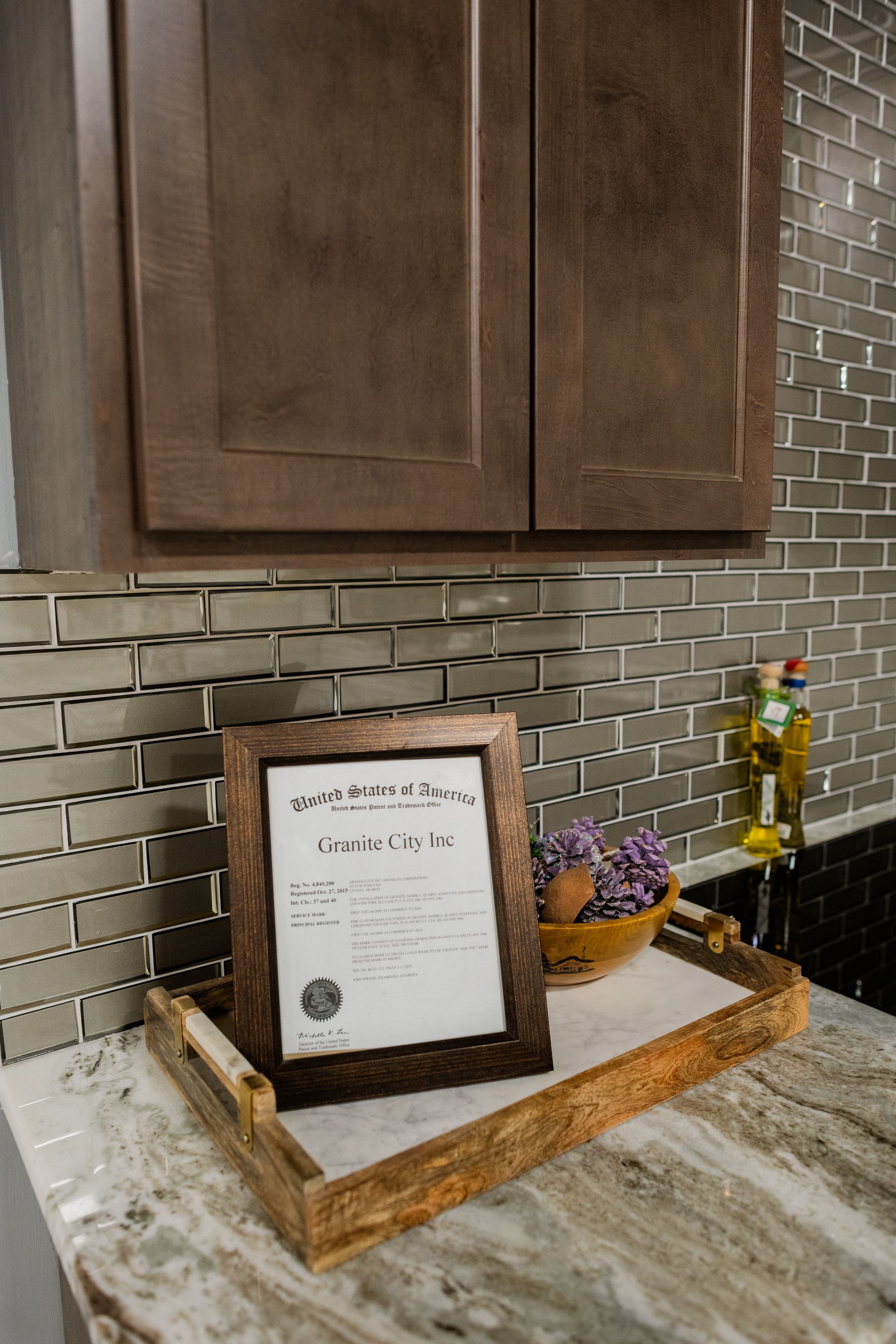 Kitchen counter with framed sign, bowl of grapes, and decorative bottles against a tile backsplash