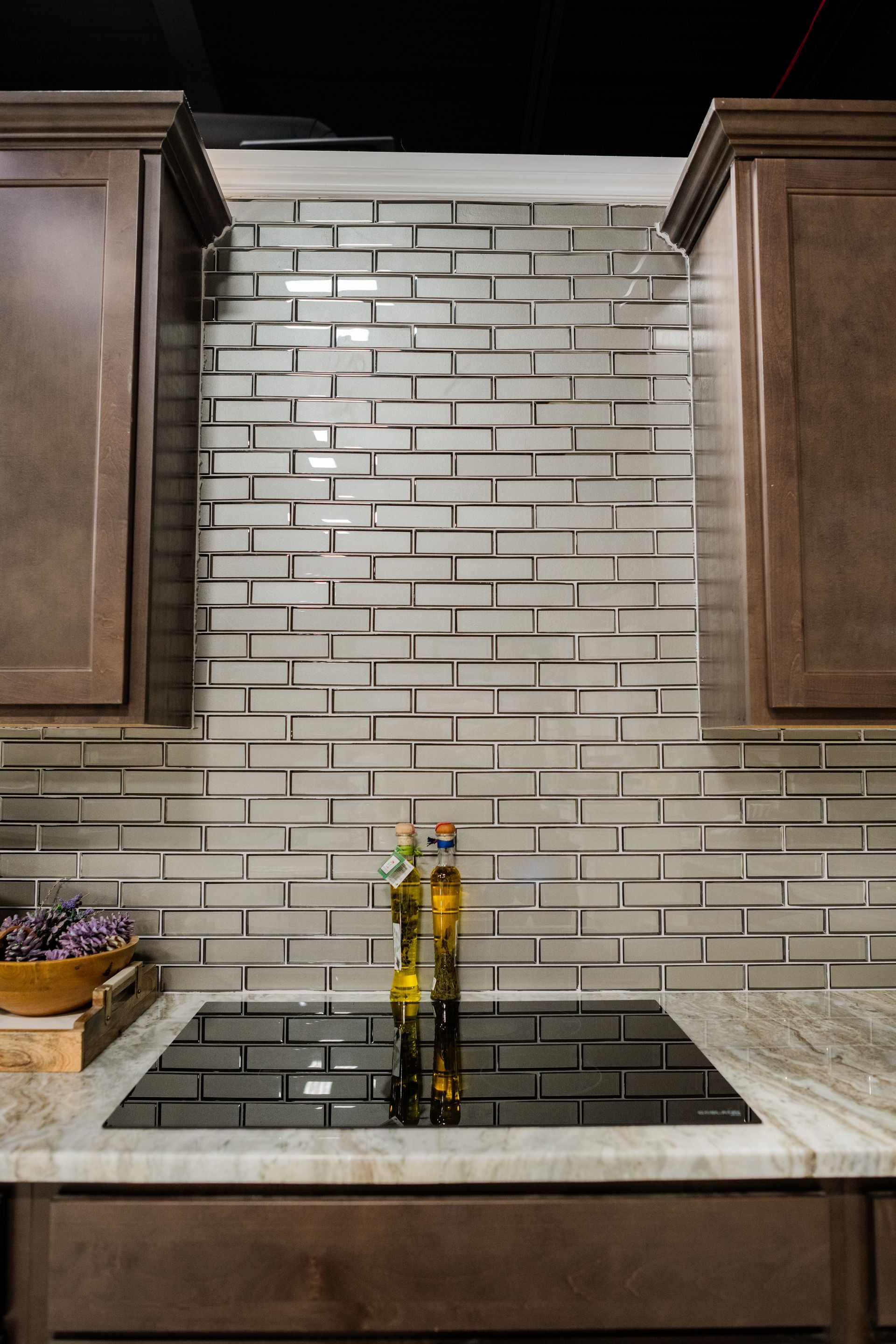 Kitchen backsplash with gray brick tile, dark cabinets, and a sink faucet centered below cabinets