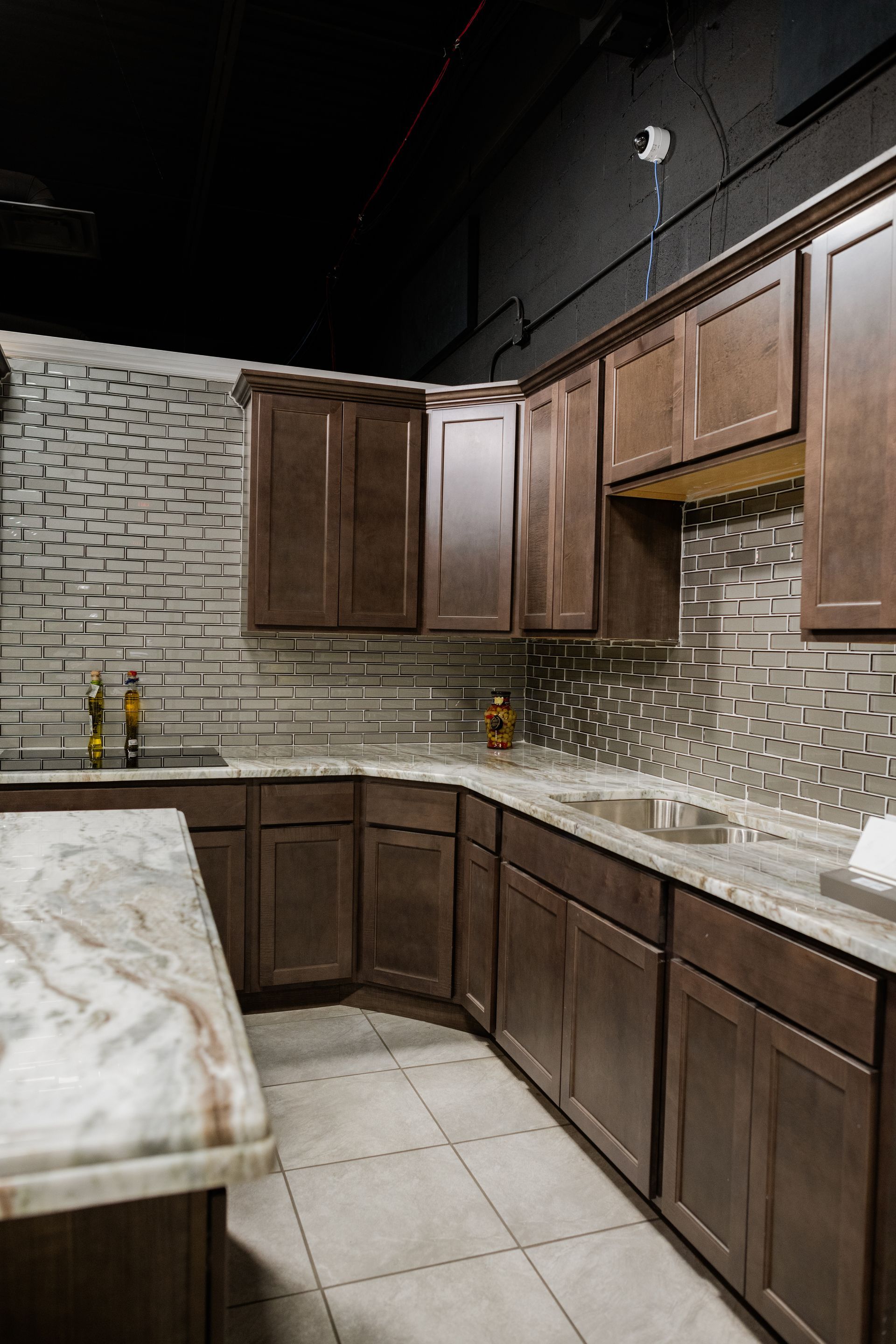Modern kitchen with dark wood cabinets, gray tile backsplash, marble countertop, and beige tile floor