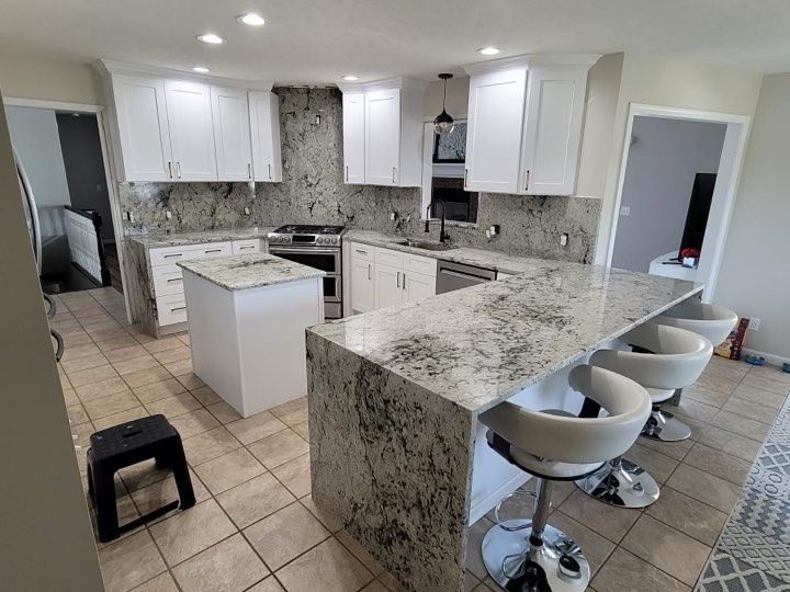 Bright white kitchen with granite island, bar stools, and tiled floor