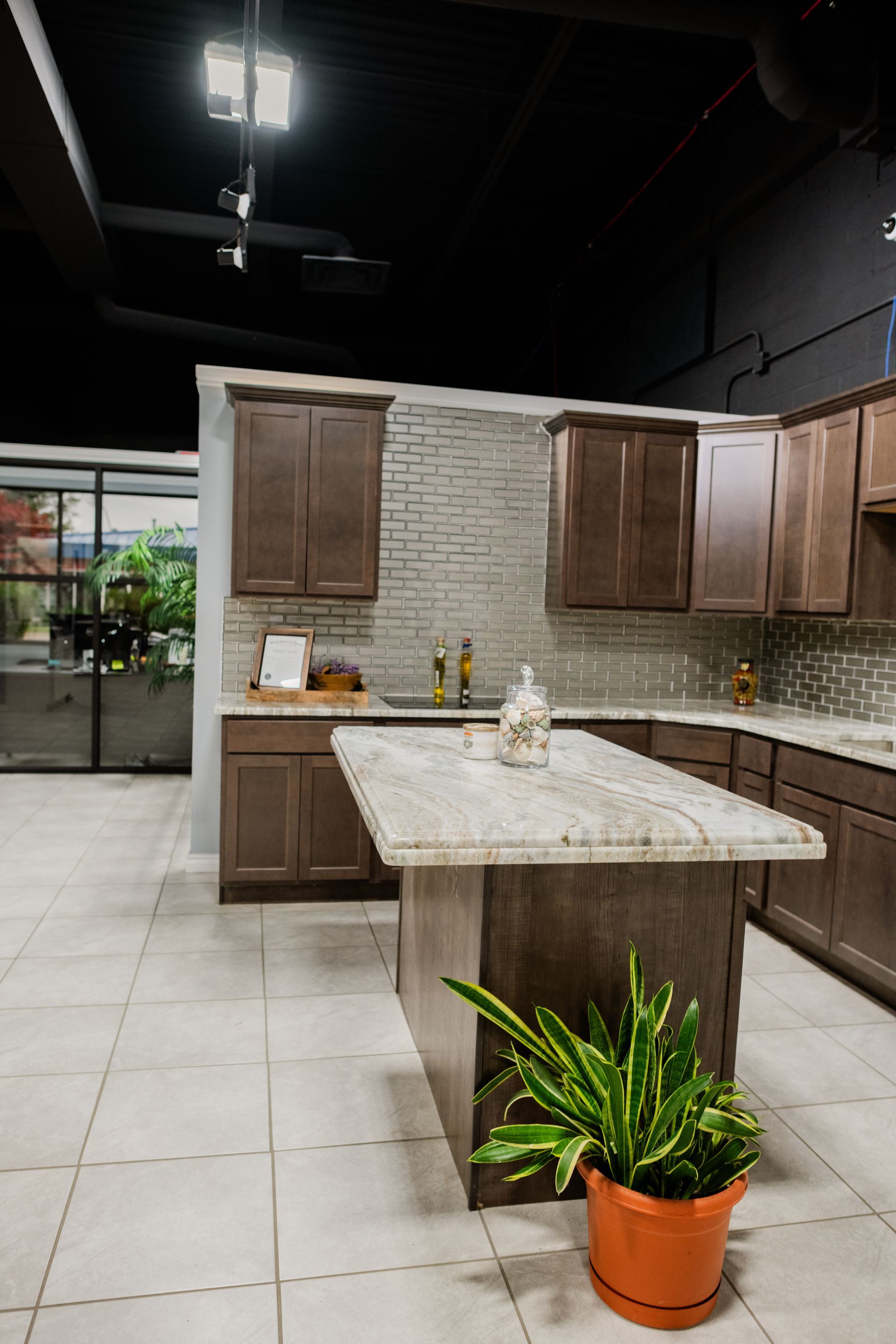 Modern kitchen with white tile floor, wood cabinets, stone island, and a potted plant in front