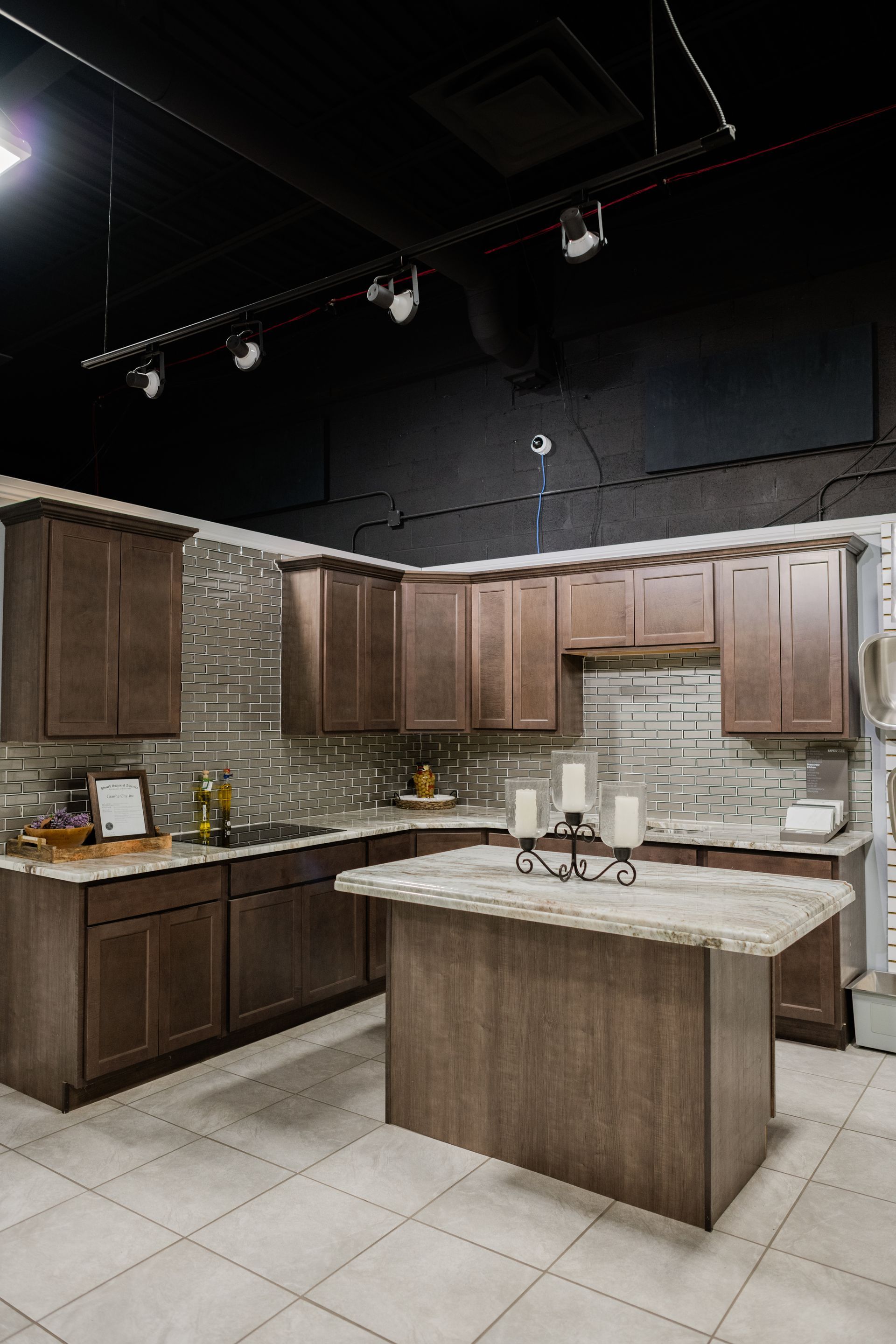 Modern kitchen with dark wood cabinets, granite island, tiled backsplash, and black track lighting