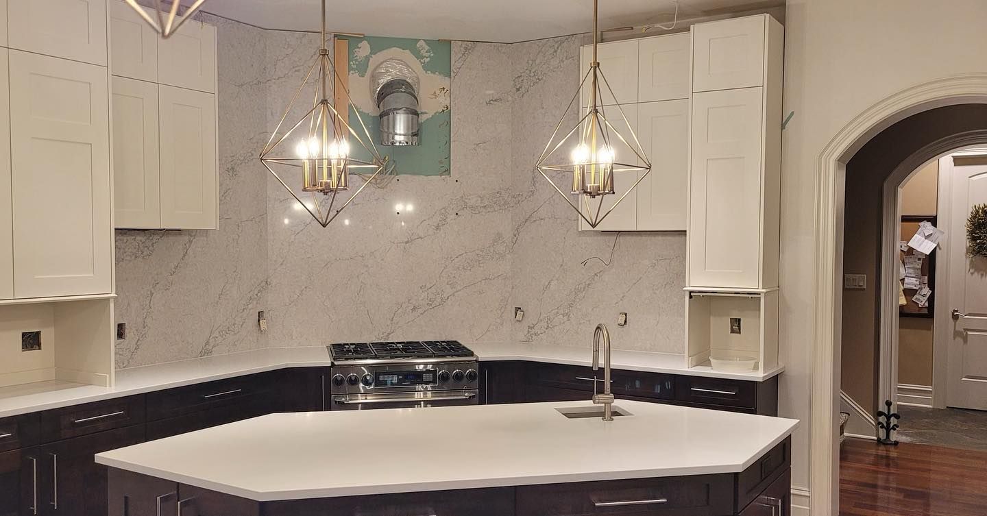 Modern white kitchen with marble backsplash, black countertops, island sink, and hanging pendant lights