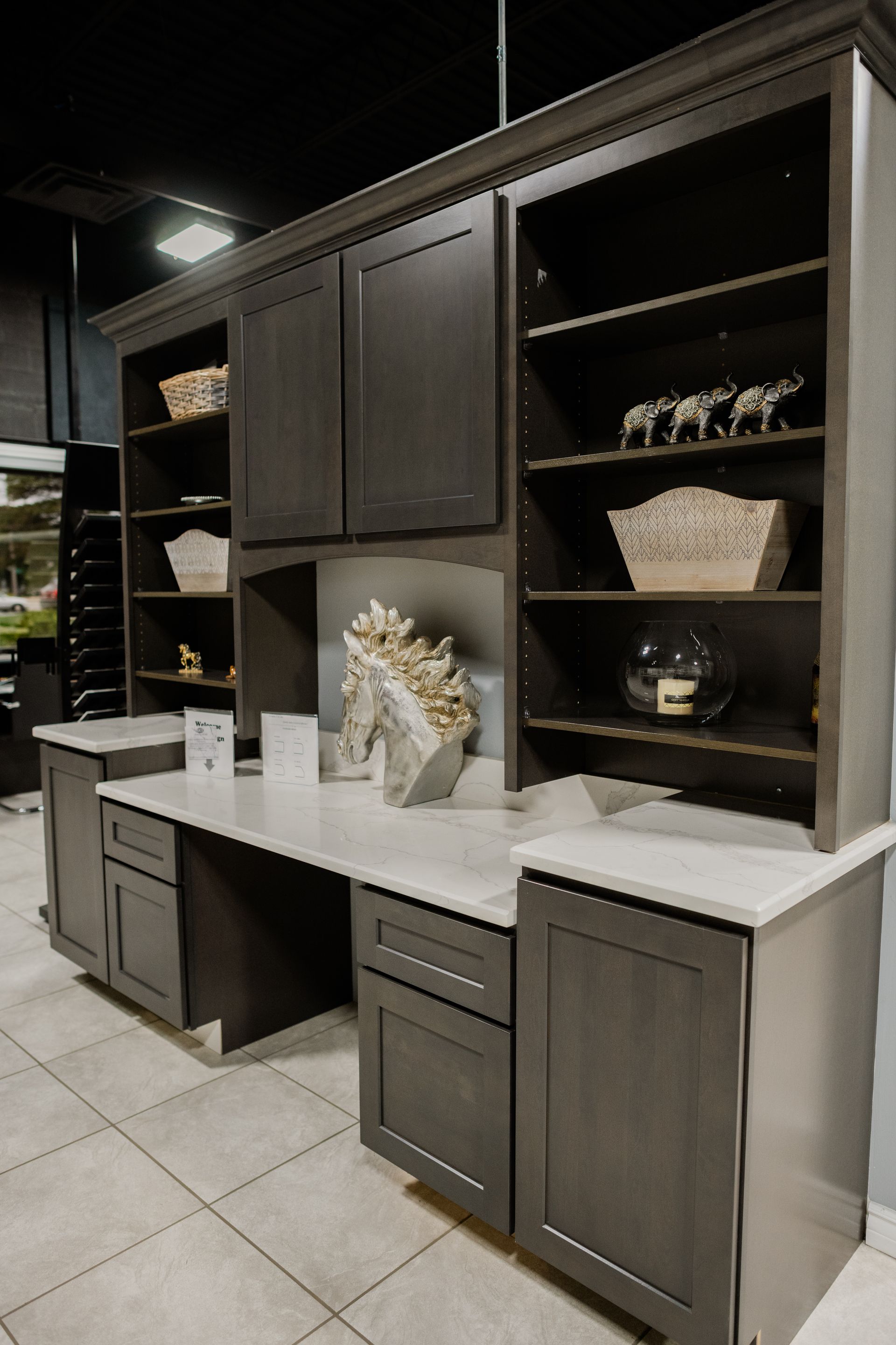 Dark wood kitchen cabinets with white countertops and open shelving in a showroom display.