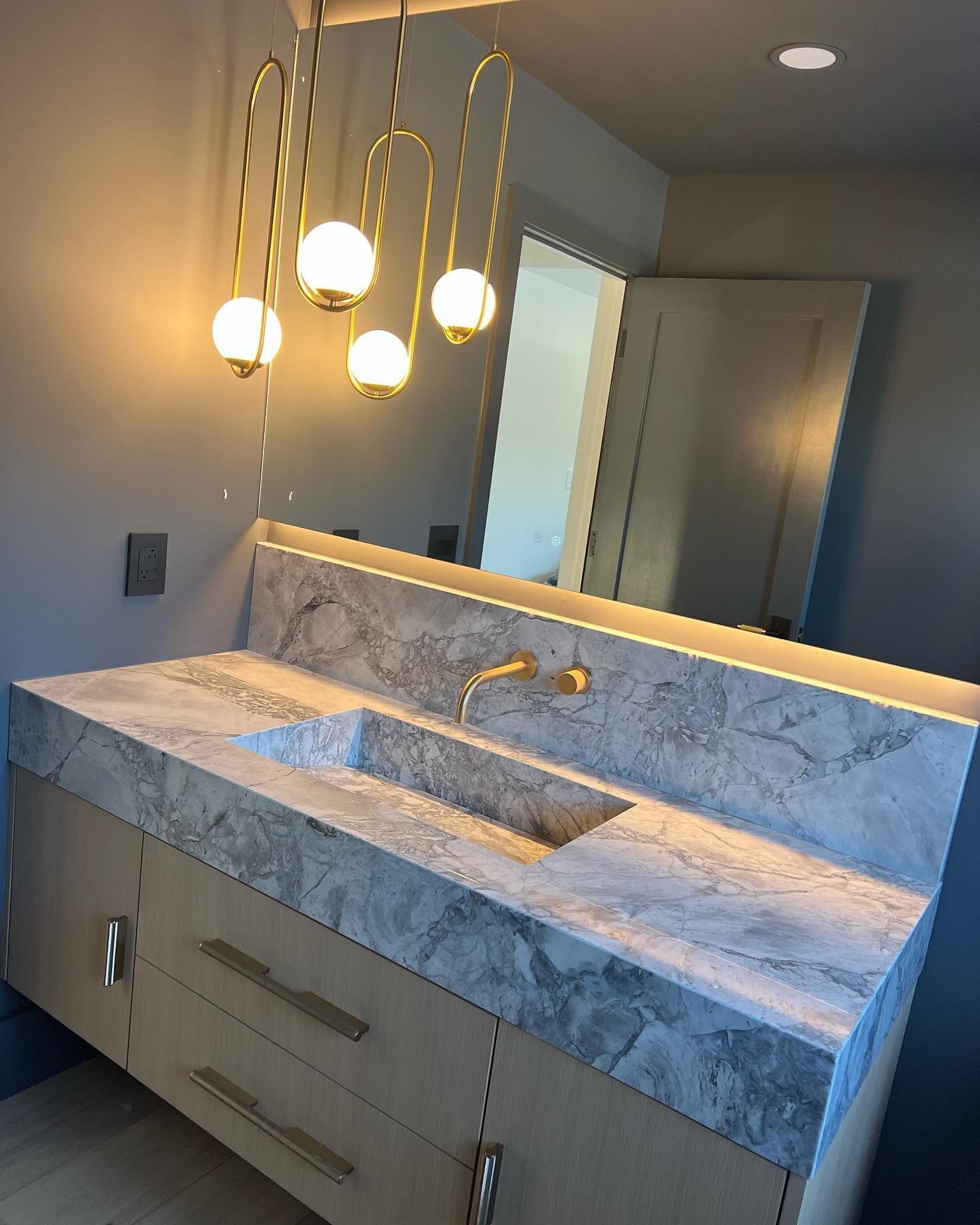 Modern bathroom vanity with marble countertop, gold pendant lights, and large mirror