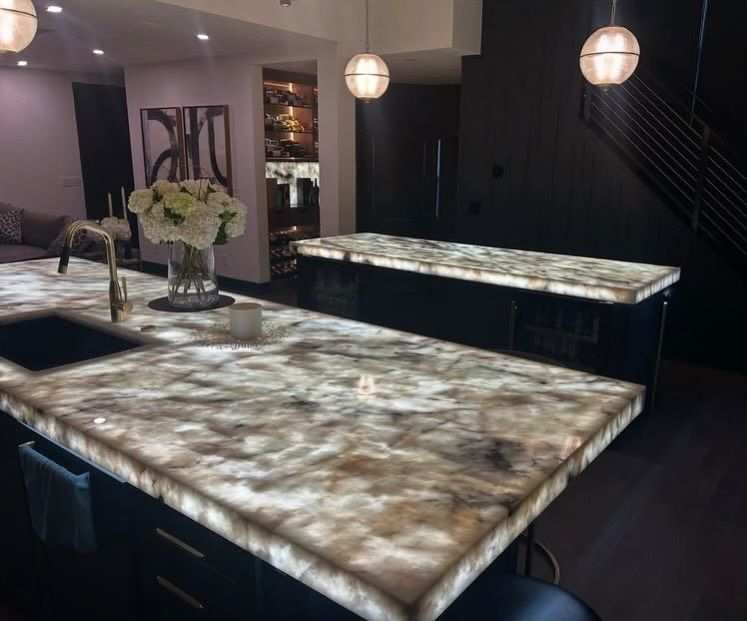 Modern kitchen with two large stone islands, dark cabinetry, and hanging pendant lights.