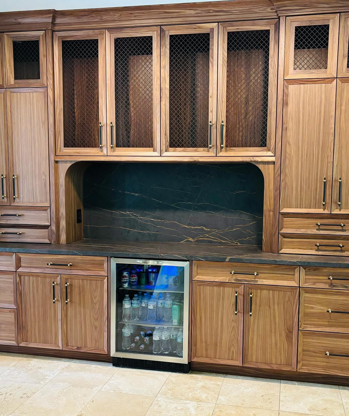Wood-paneled kitchen cabinetry with glass-front uppers, central niche, and a small built-in beverage cooler below.