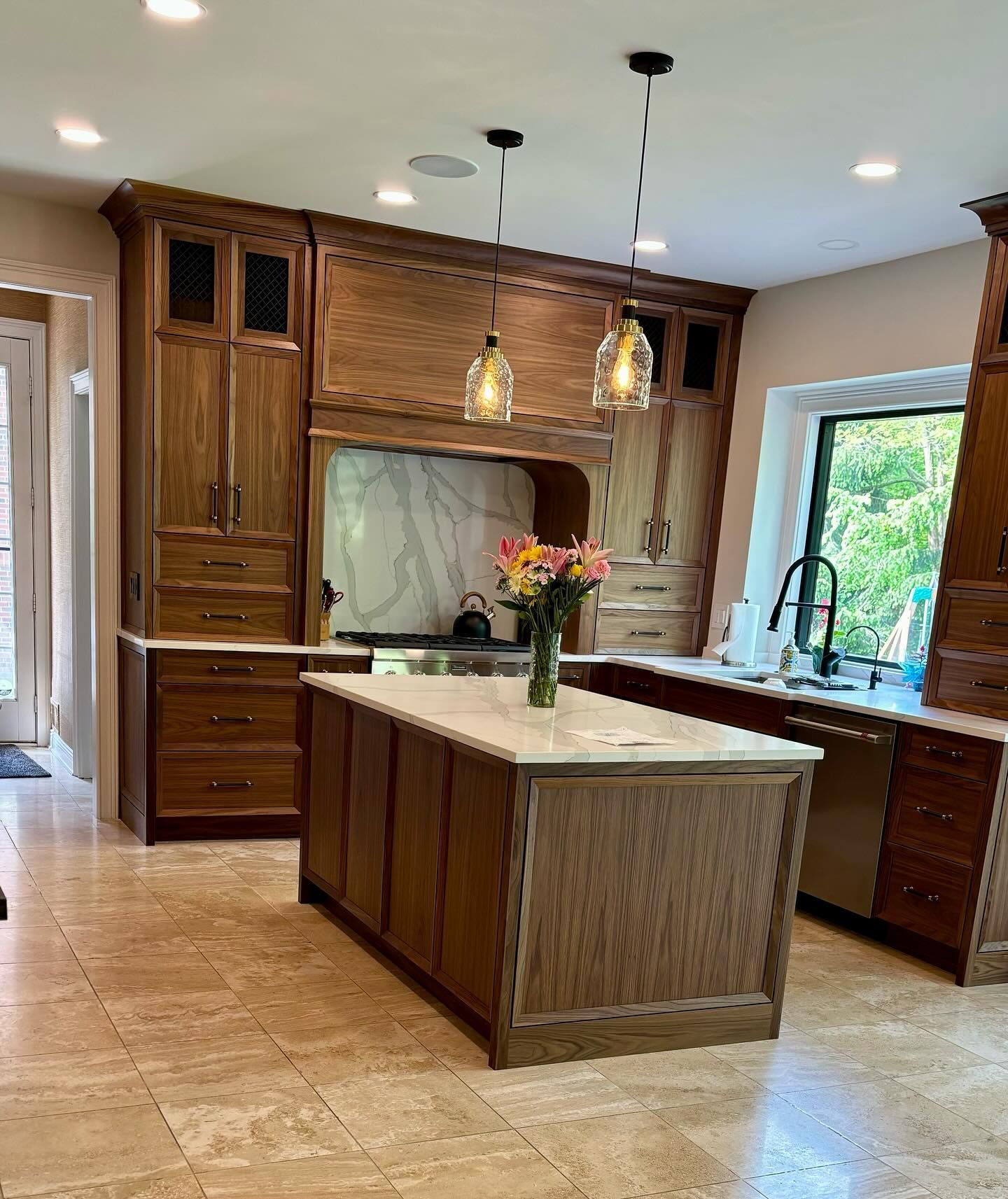 Spacious kitchen with wood cabinets, large island, pendant lights, and a vase of flowers by the sink.