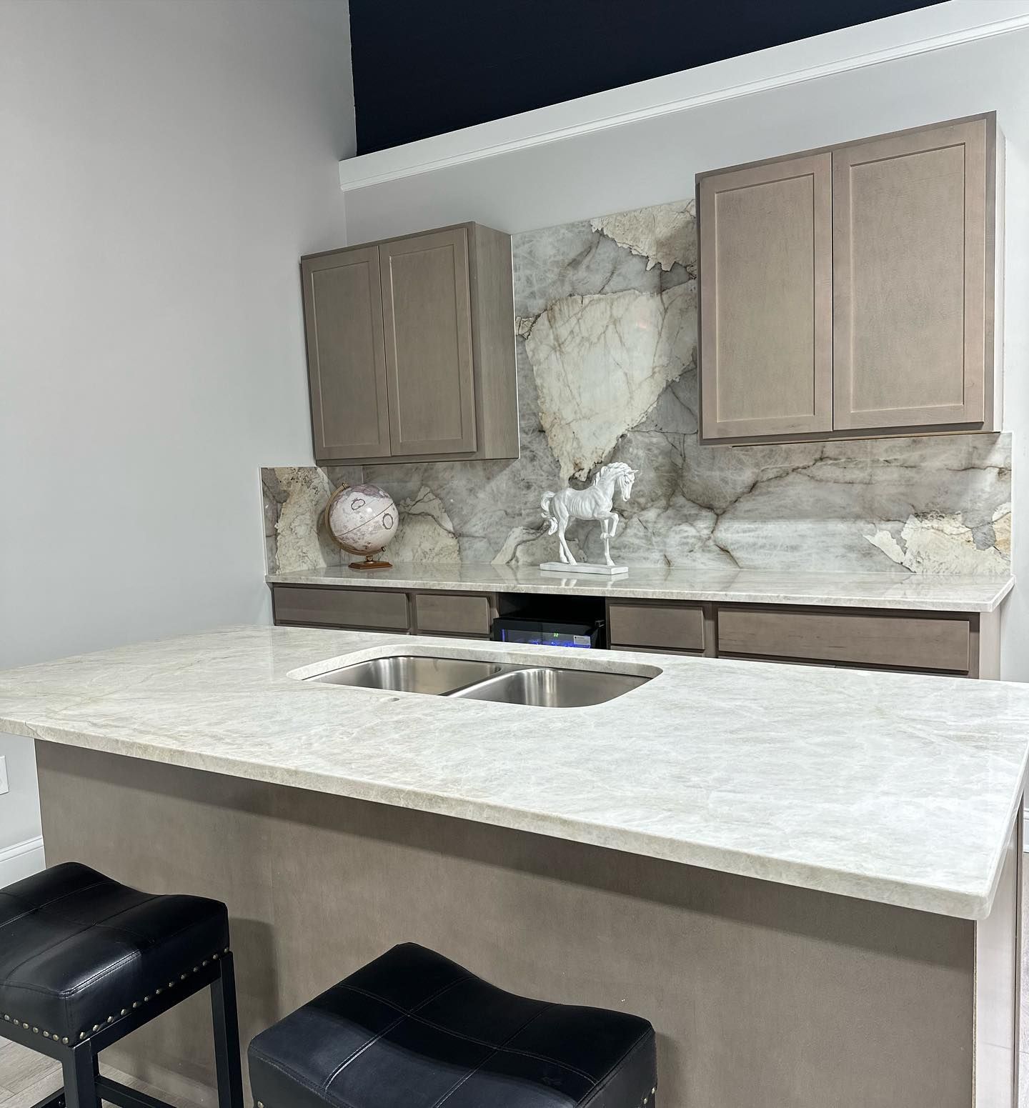 Modern kitchen bar with marble island, double sink, and light wood cabinets.