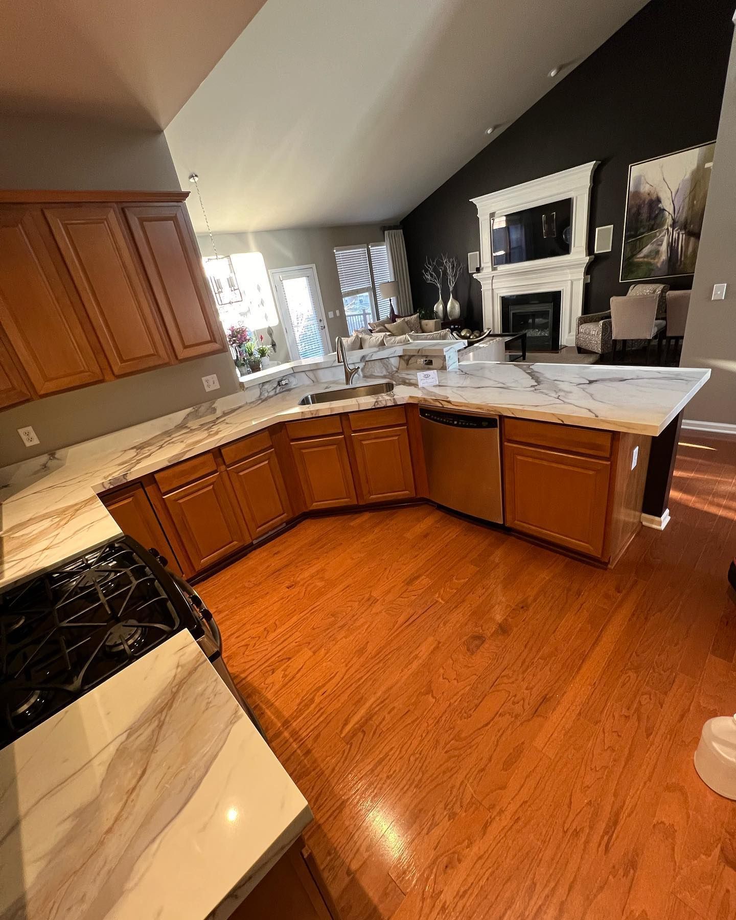 Modern kitchen with wood cabinets, marble island, dark accent wall, and hardwood floors