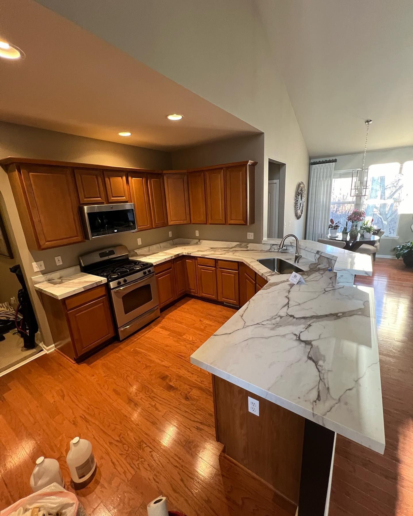 Modern kitchen with wood cabinets, marble island, and hardwood floors, opening to a bright living area