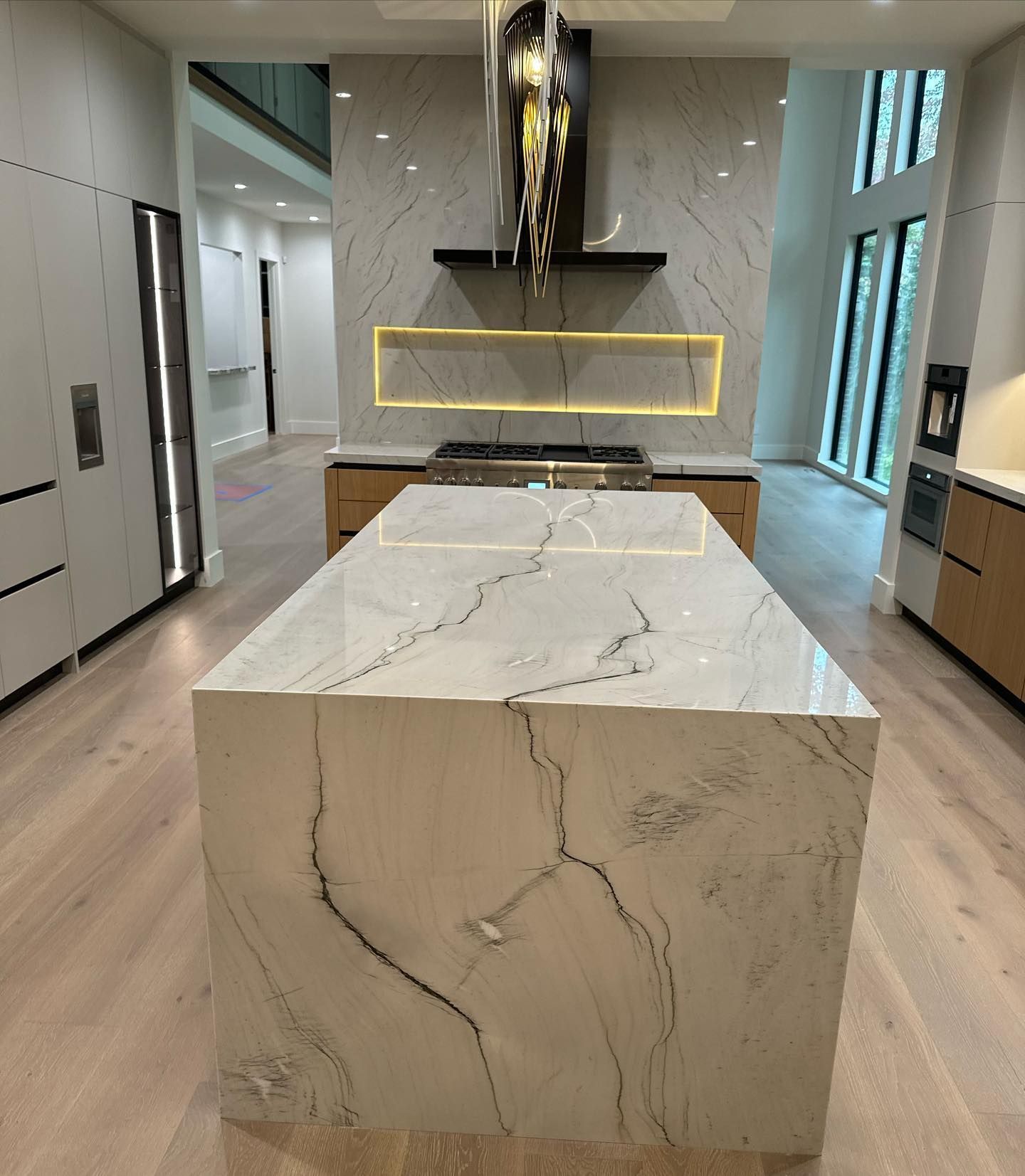 Modern kitchen with a white marble island and brass-accented range hood in a bright hallway-like space