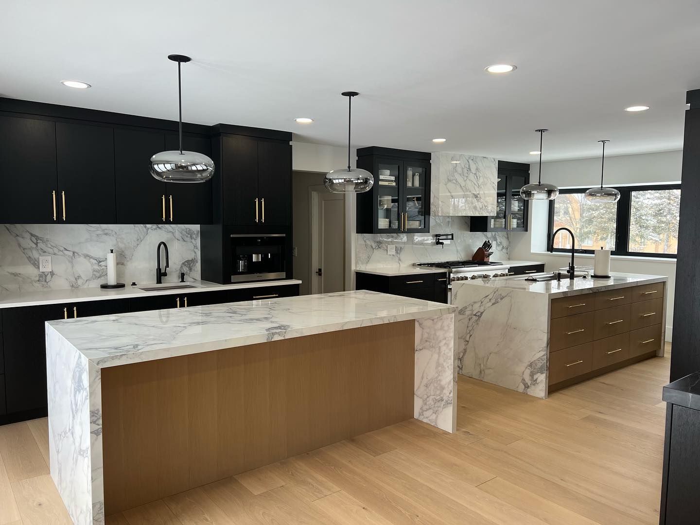 Modern kitchen with black and white cabinetry, marble islands, and light wood flooring