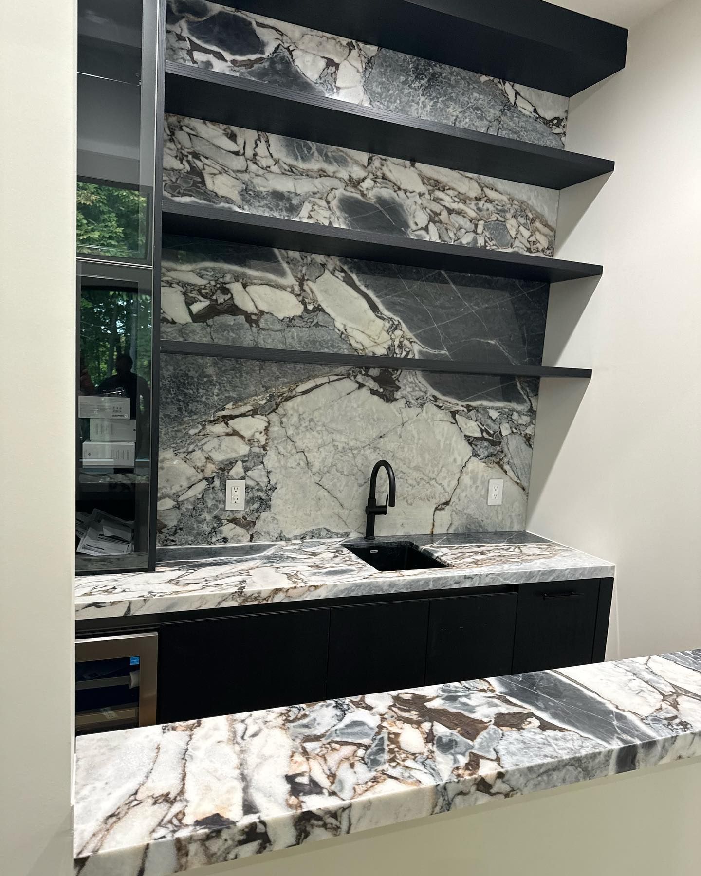 Modern kitchen with marble waterfall counter, open shelves, and black sink under stone-patterned backsplash