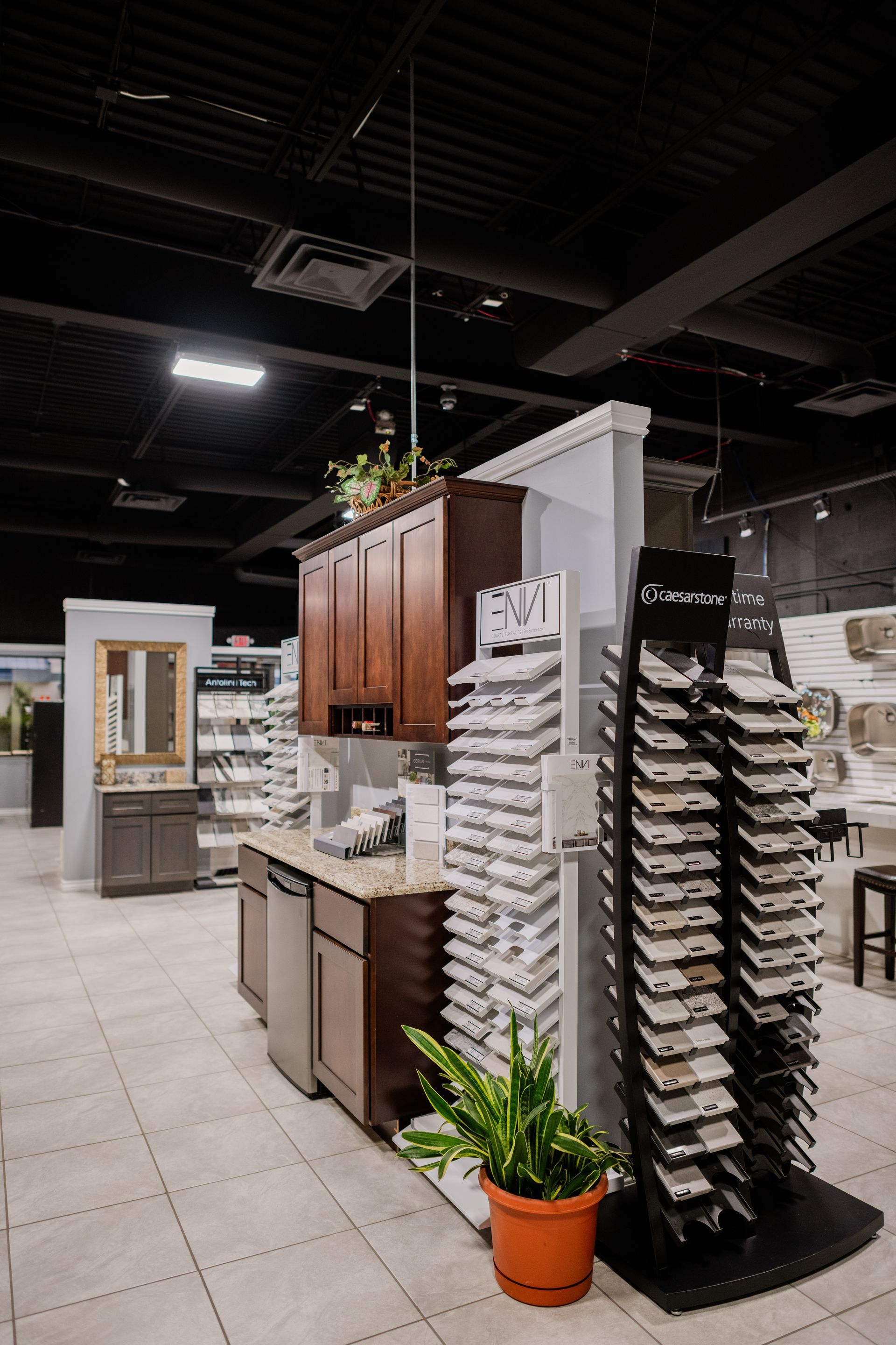 Flooring showroom with tile displays, sample racks, and a potted plant under bright overhead lights
