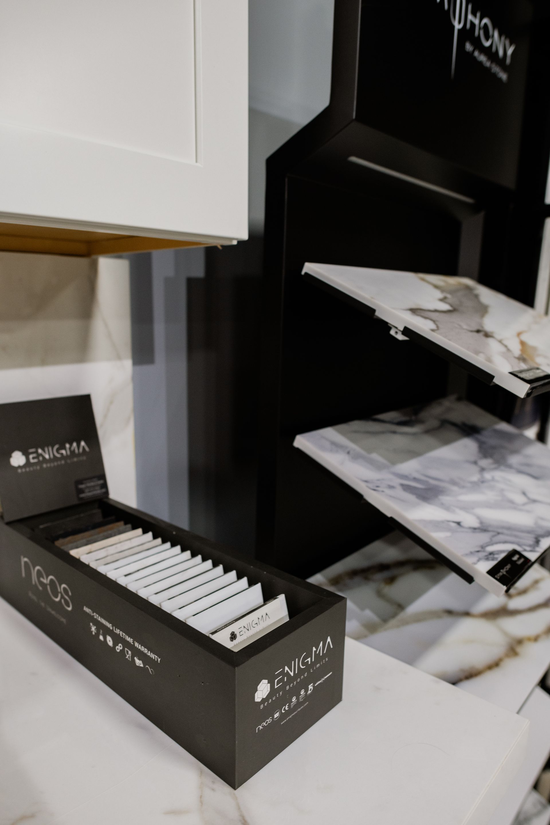 Black countertop display with rows of sample tiles beside a shelf of marble stone slabs